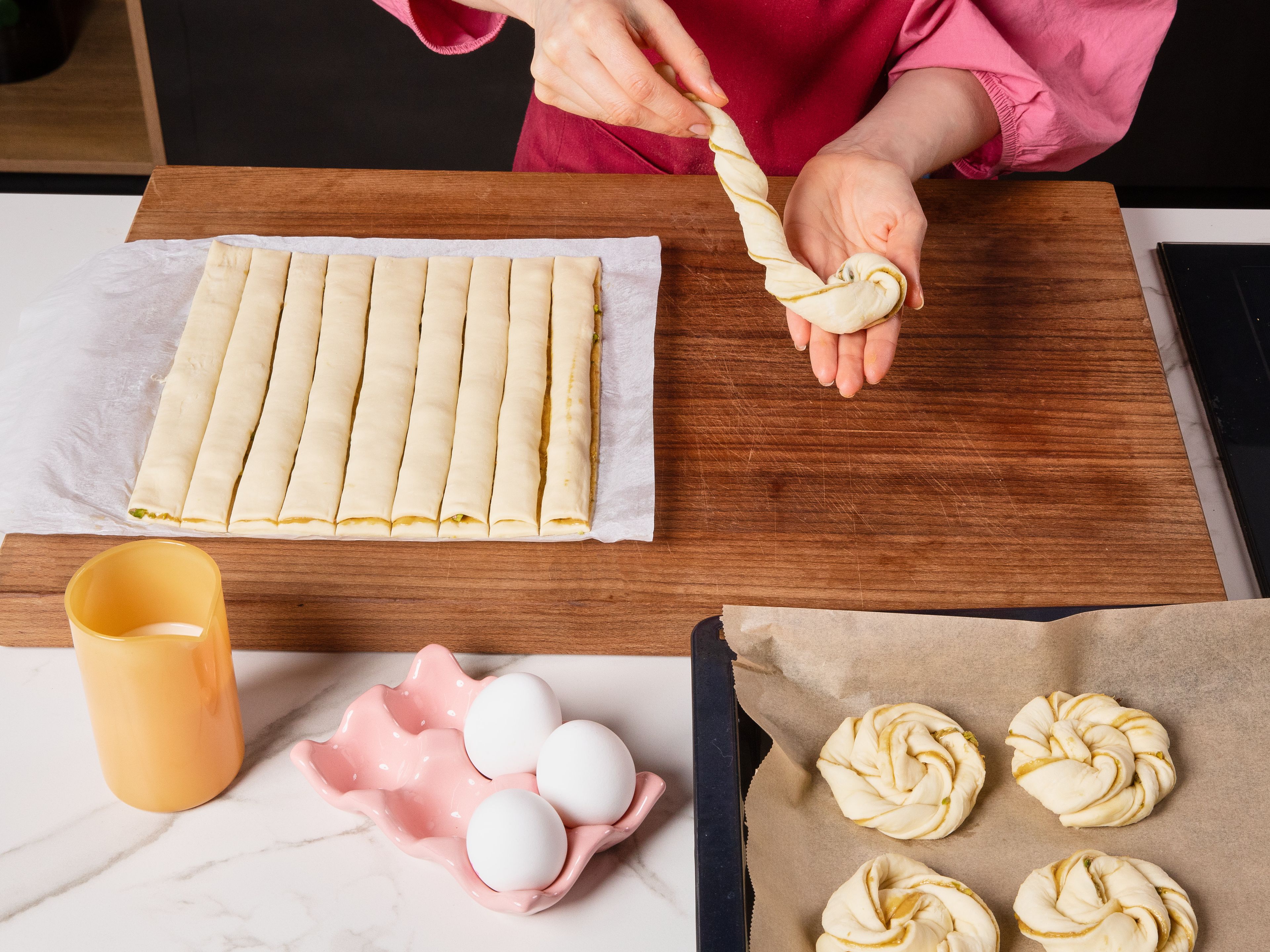 Den gefüllten Teig mit einem Pizzaschneider oder einem Messer in ca. 2 cm breite Streifen schneiden. Jeden Streifen vorsichtig von der Arbeitsfläche lösen, von beiden Seiten in entgegengesetzte Richtungen eindrehen und zu einem lockeren Nest aufrollen. Die Nester auf ein mit Backpapier belegtes Backblech legen. Das Ei mit der Milch verquirlen und die Nester damit bestreichen.