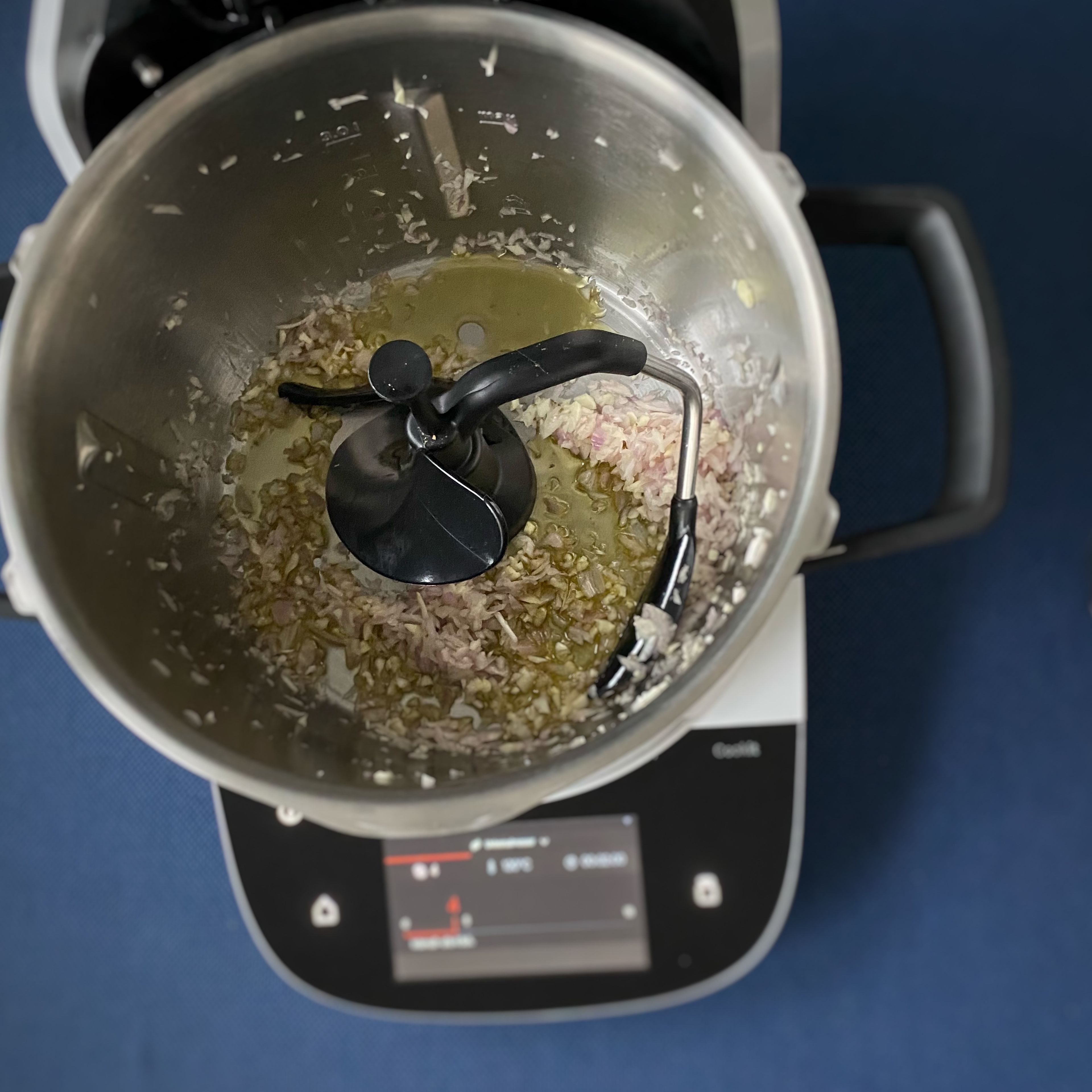 Das Cookit Universalmesser einsetzen. Die Schalotten und den Knoblauch schälen und in den Cookit geben. Den Deckel schließen, Messbecher einsetzen und zerkleinern (Universalmesser | Stufe 14 | 10 Sekunden). Die Zutaten mit dem Cookit Küchenspatel nach unten schieben. Das Universalmesser entfernen und den 3D-Rührer einsetzen. Öl hinzufügen.