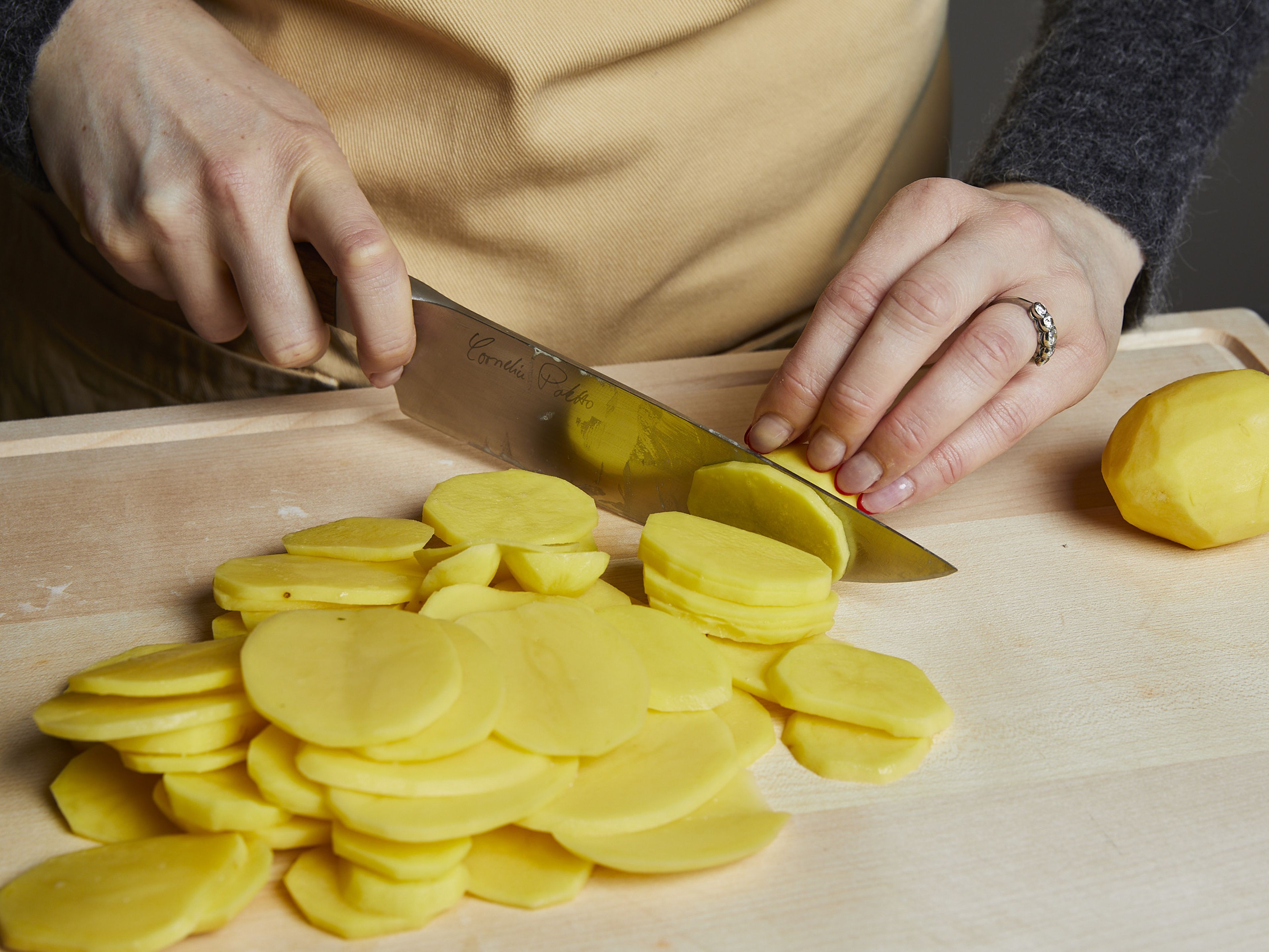 Den Backofen auf 210°C Ober-/Unterhitze vorheizen. Zwiebel und Knoblauch fein würfeln und beiseitestellen. Kartoffeln schälen und mit einer Mandoline oder einem Messer in sehr dünne Scheiben schneiden.