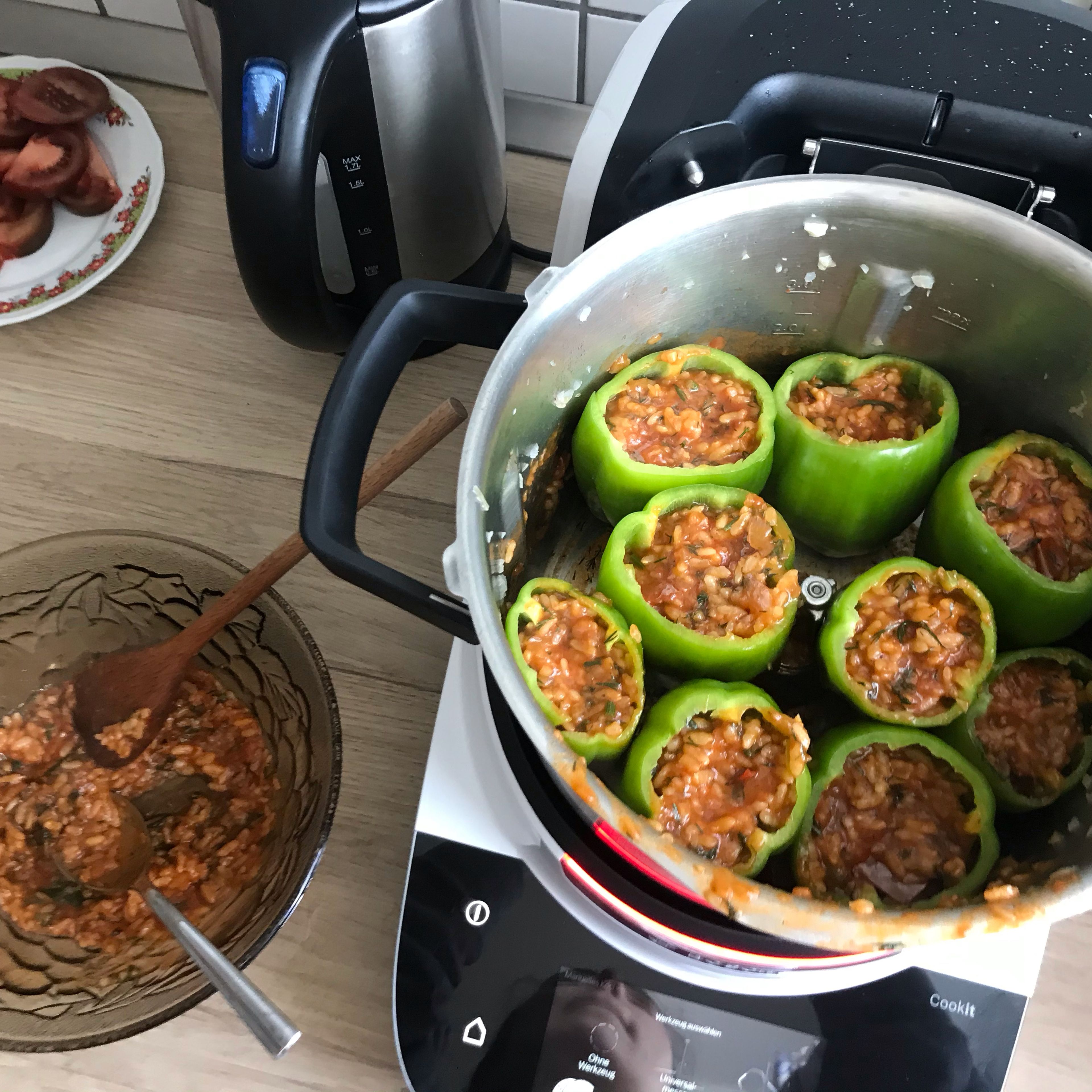 Den Topfinhalt in eine Schüssel geben, den Dill einrühren und die Paprikas damit befüllen, danach in den Topf stellen. Die zweite Tomate in 9 Stücke schneiden, sodass sie auf die Paprika passen. Erst die Tomatenscheiben danach die Hauben auf die Paprikas drauflegen und kochen lassen. (Ohne Werkzeug|98 Grad|15 Minuten). Anschließend auf dem Teller mit Jogurt servieren.