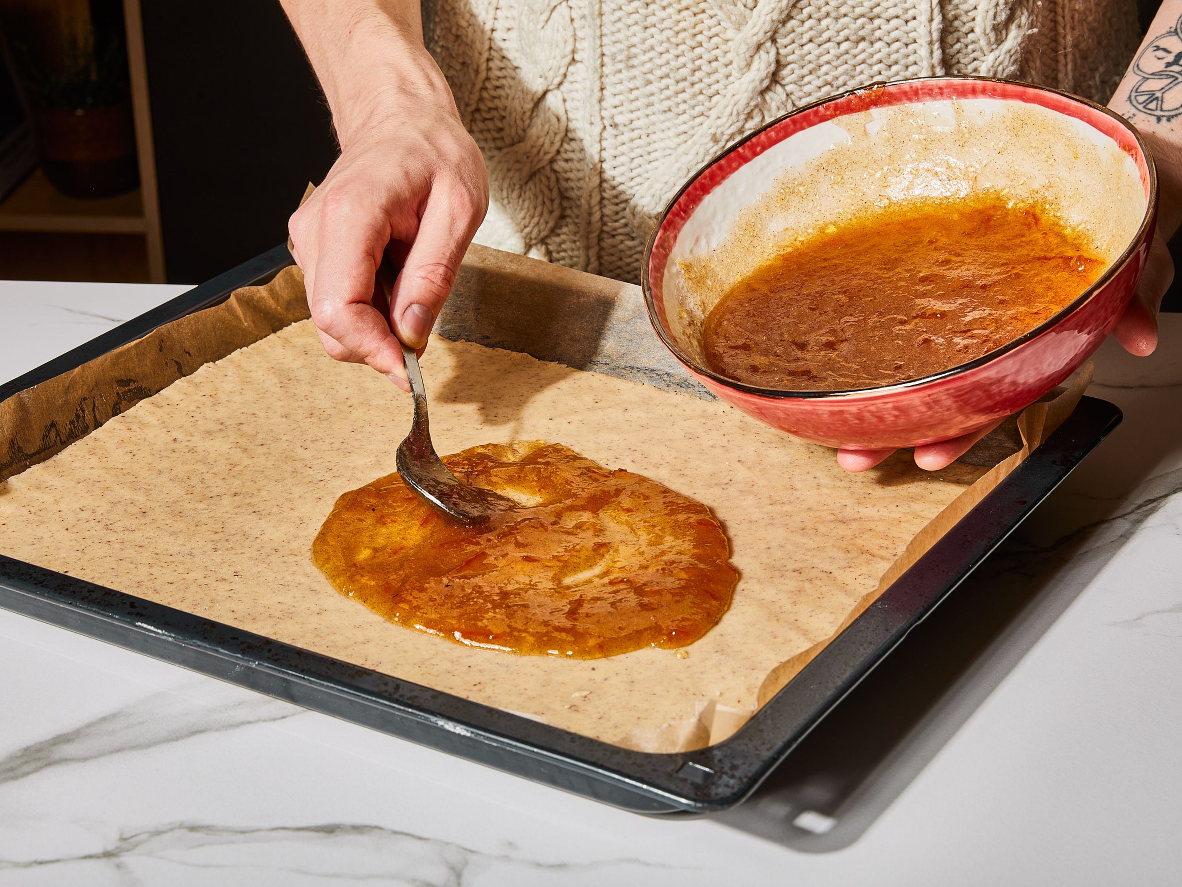 Ofen auf 175°C/347°F Ober-/Unterhitze vorheizen. In einer mittleren Schüssel Orangenmarmelade mit Kardamom, Zimt und Salz glatt rühren. Den vorbereiteten Teig 1 cm dick auf einem mit Backpapier belegten Backblech verteilen und gleichmäßig platt drücken, dabei etwas Teig für die Dekoration zurückbehalten. Die gewürzte Orangenmarmelade dünn auf der Teigoberfläche verstreichen.