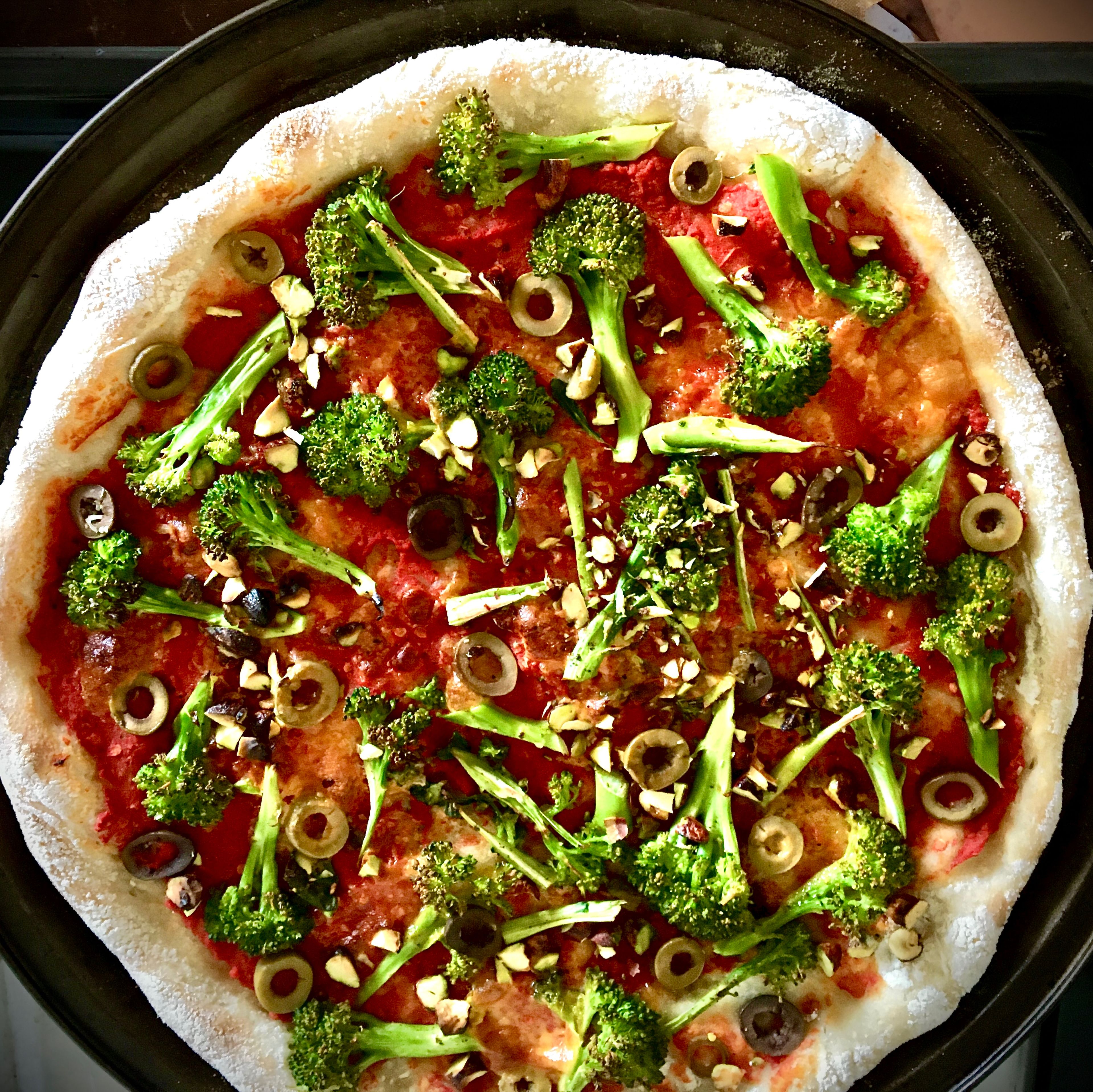 Repeat shape&stretch step with remaining dough. Place onto the second baking dish. Spread tomato sauce over and drizzle with olive oil. Arrange broccoli, remaining olives and pistachios on top. Bake for 8-10 min. Cool a bit, then dollop the pesto sauce here and there.