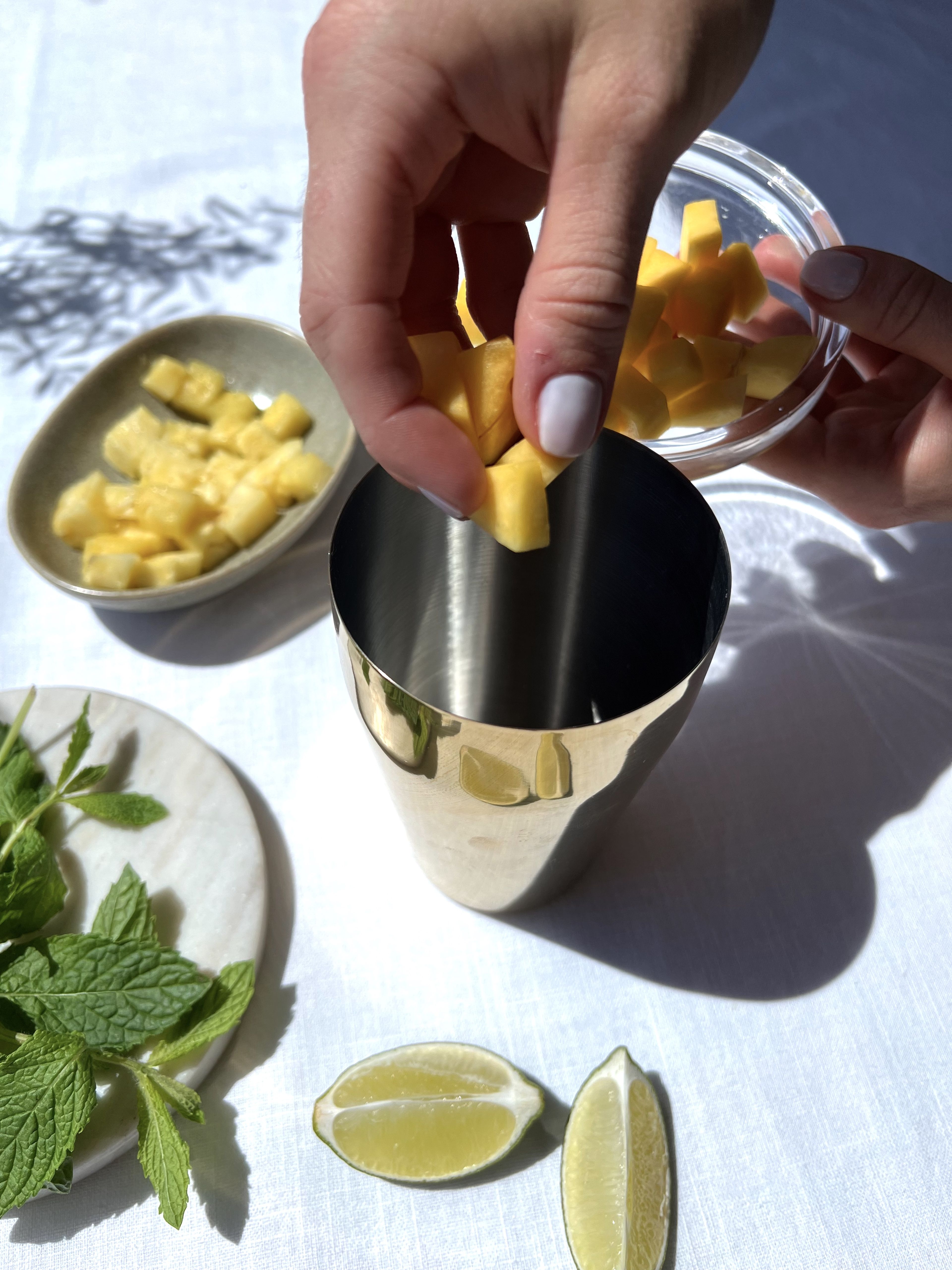 Mango, Ananas, Minze und braunen Zucker in einen Shaker geben und mit Stößel muddeln.