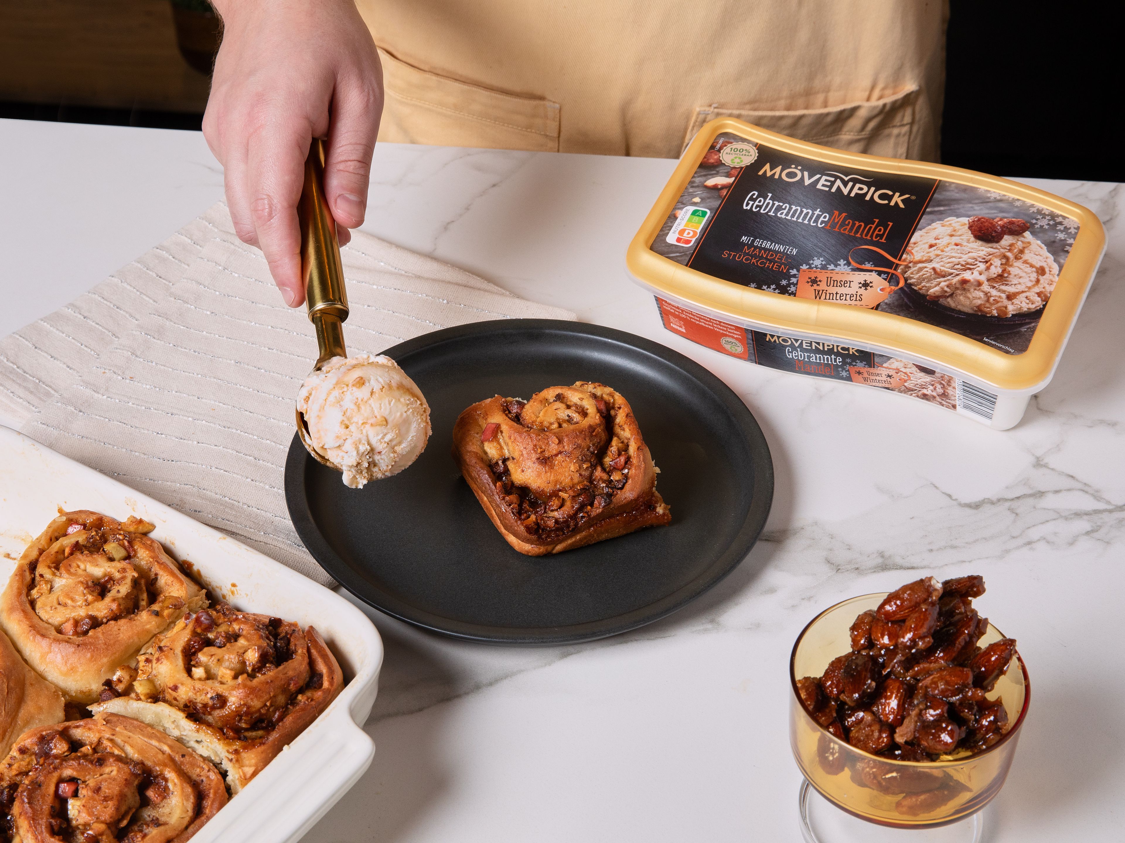Den Backofen auf 170 °C (Ober-/Unterhitze) vorheizen. Den Teig von der Längsseite her aufrollen und in ca. 4 cm breite Stücke schneiden. Die Teigschnecken in die gefettete Backform setzen. Ca. 30 Min. backen, bis sie goldbraun sind. Herausnehmen, etwas abkühlen lassen und mit Mövenpick Gebrannte Mandel Eis servieren. Mit den beiseitegelegten gebrannten Mandeln bestreuen.