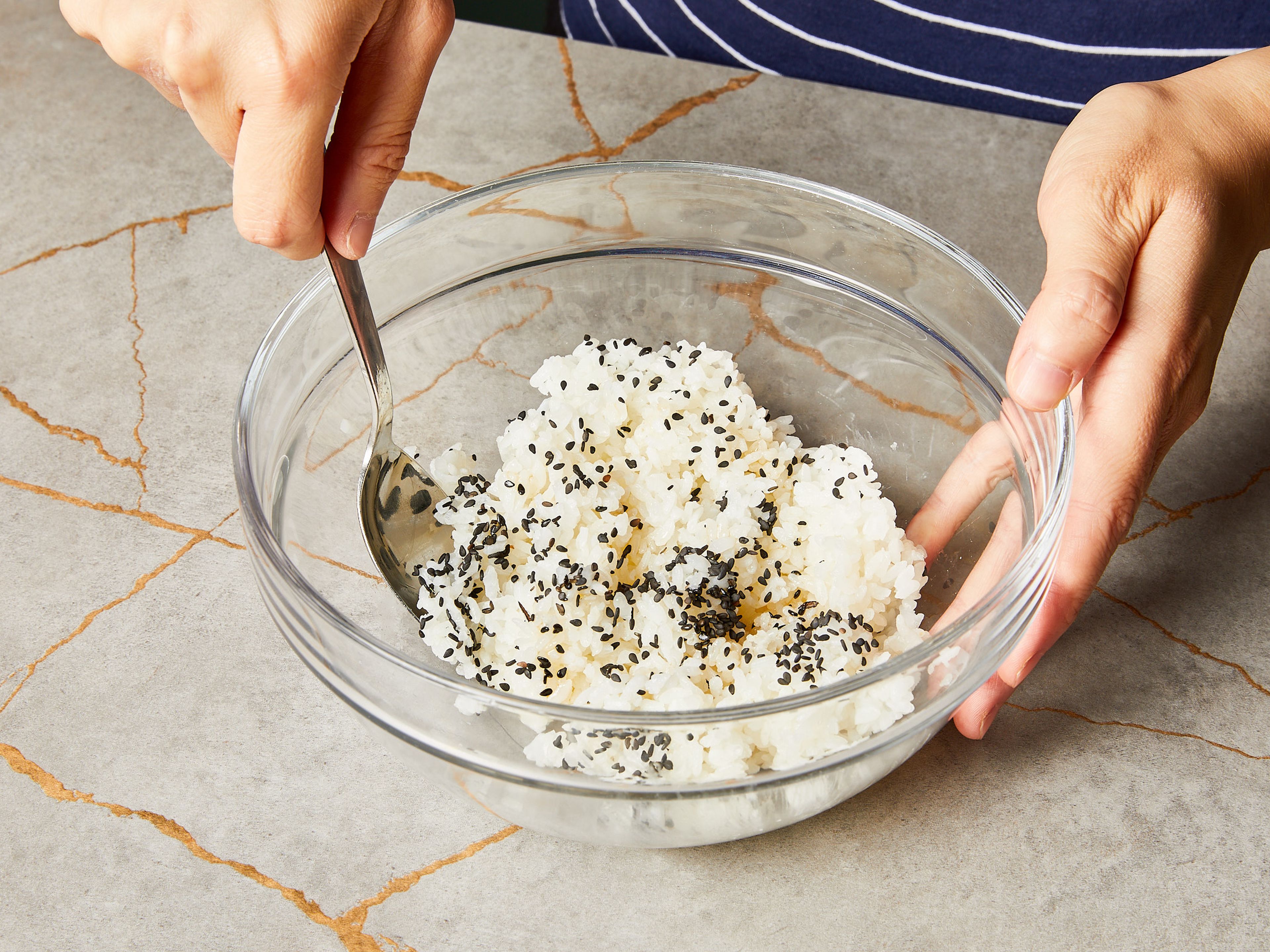 Den gekochten Sushireis abkühlen lassen dann und mit der Hälfte des Sesamöls, schwarzem Sesam und einer Prise Salz in einer Schüssel vermengen.