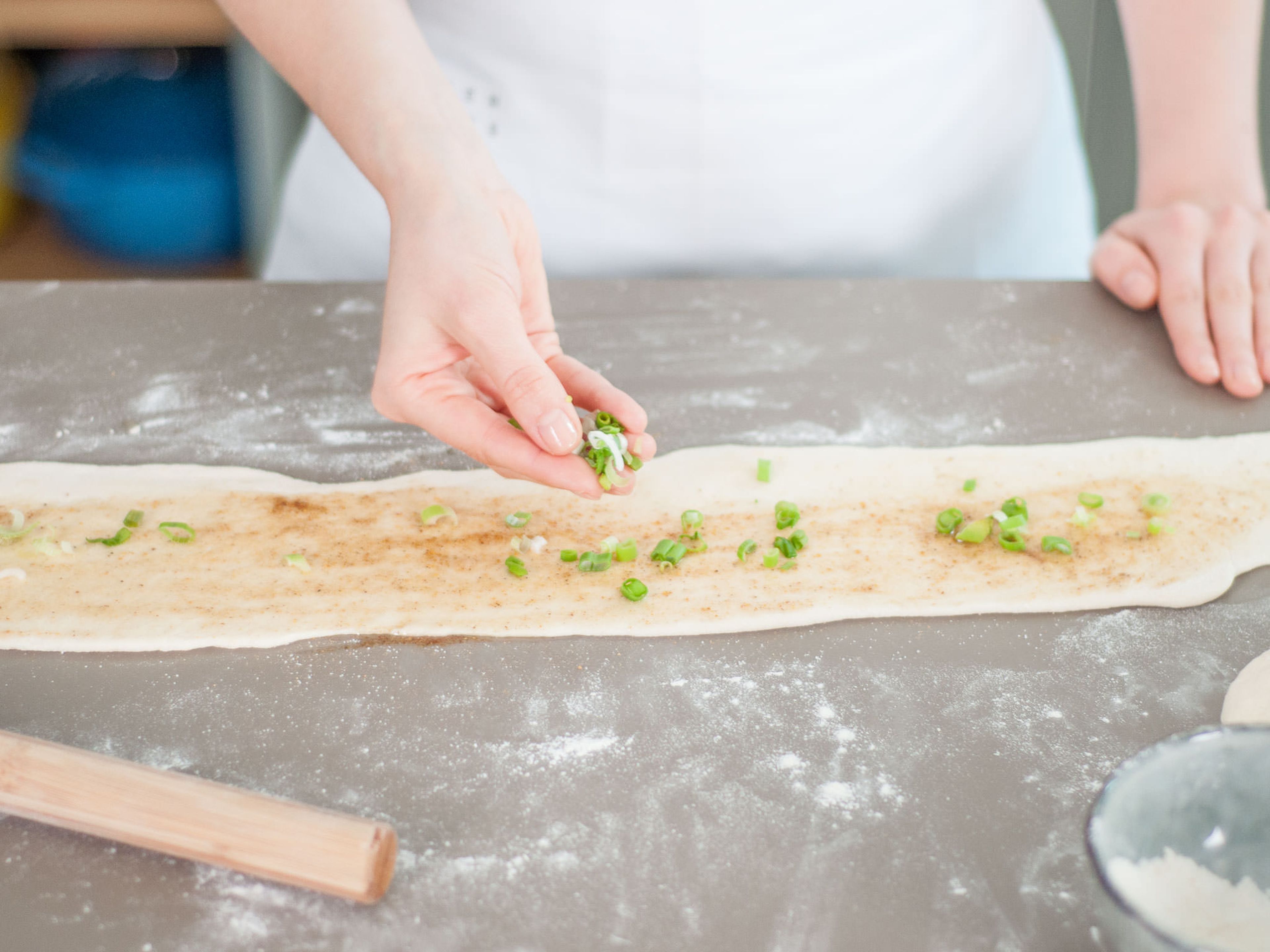 Divide dough in half and flour a work surface. Roll each piece of dough into a long, thin strip and coat with a small spoonful of scallion-infused oil, five spice powder, and salt. Sprinkle remaining chopped scallions on top, reserving some for garnishing.