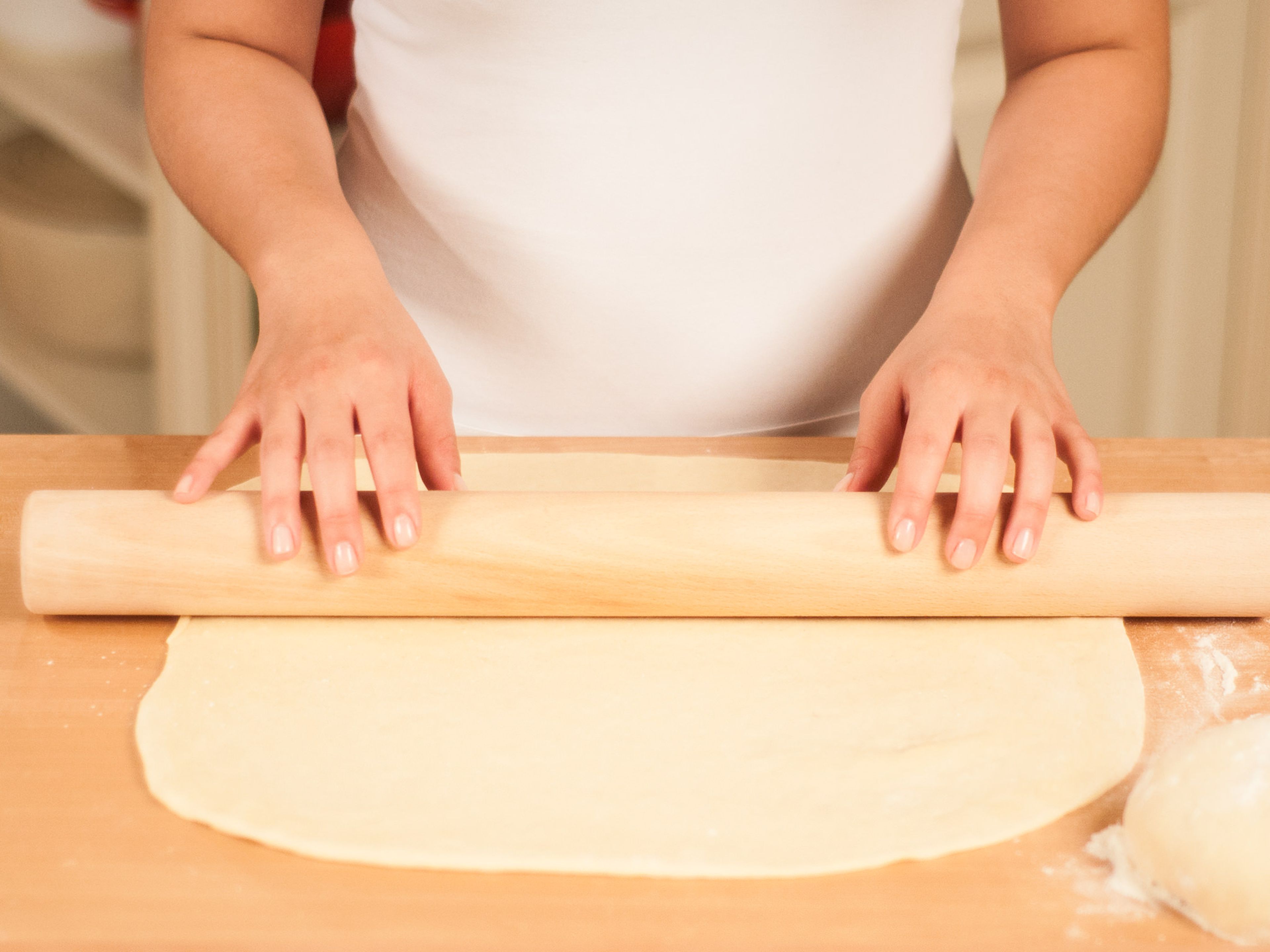 Once the dough has risen, dust a clean working surface with flour and place the dough on it. Cut the dough in half and roll each half into the shape of a rectangle, approx. 3 mm thick.
