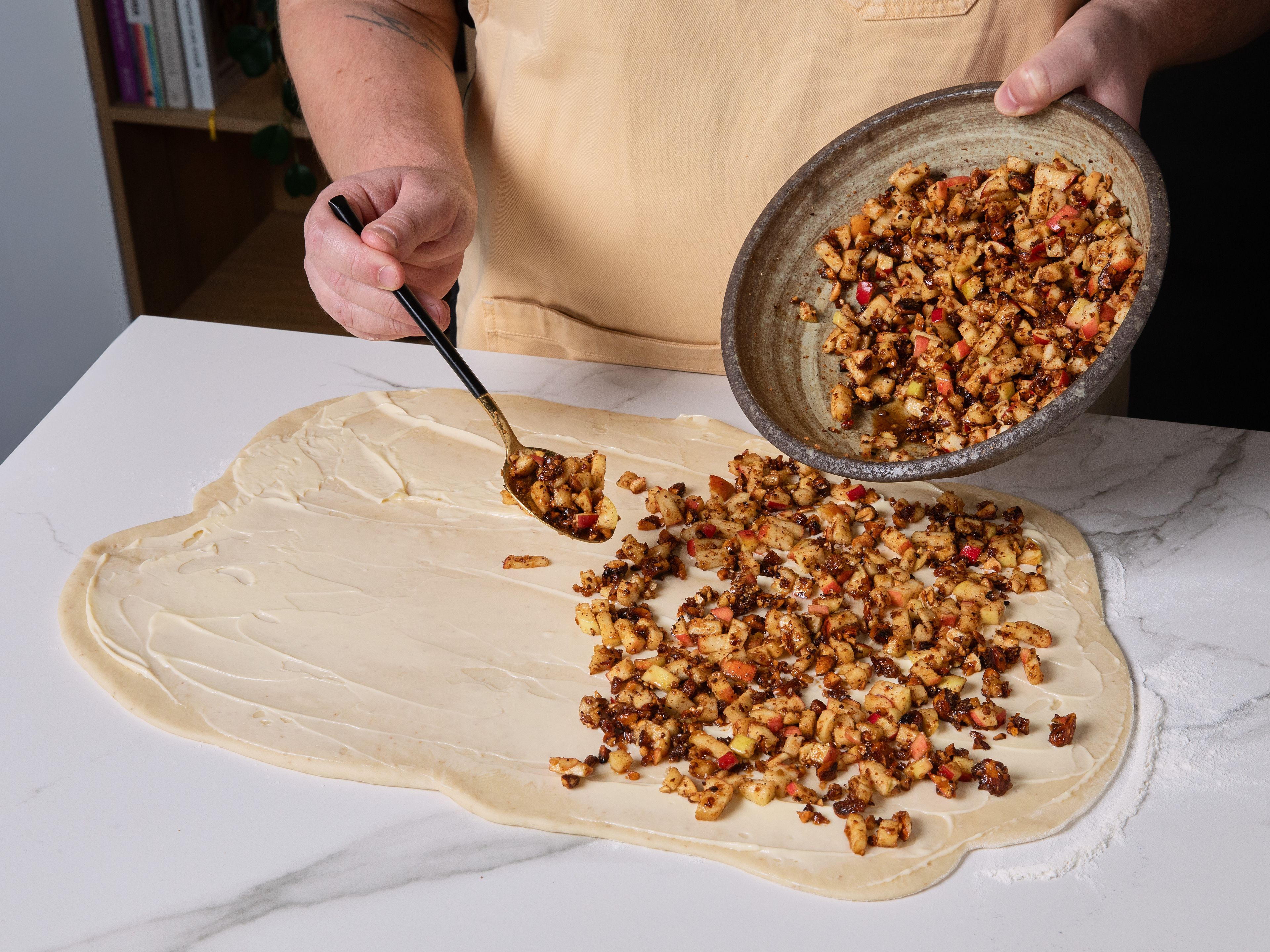 Eine Backform mit Butter einfetten. Die Arbeitsfläche leicht mit Mehl bestäuben und den Teig zu einem Rechteck ausrollen, bis er ca. 7 mm dick ist. Mit der restlichen weichen Butter bestreichen, dann die Apfel-Mandel-Mischung gleichmäßig darauf verteilen. Braunen Zucker und den restlichen Zimt mischen und darüberstreuen.