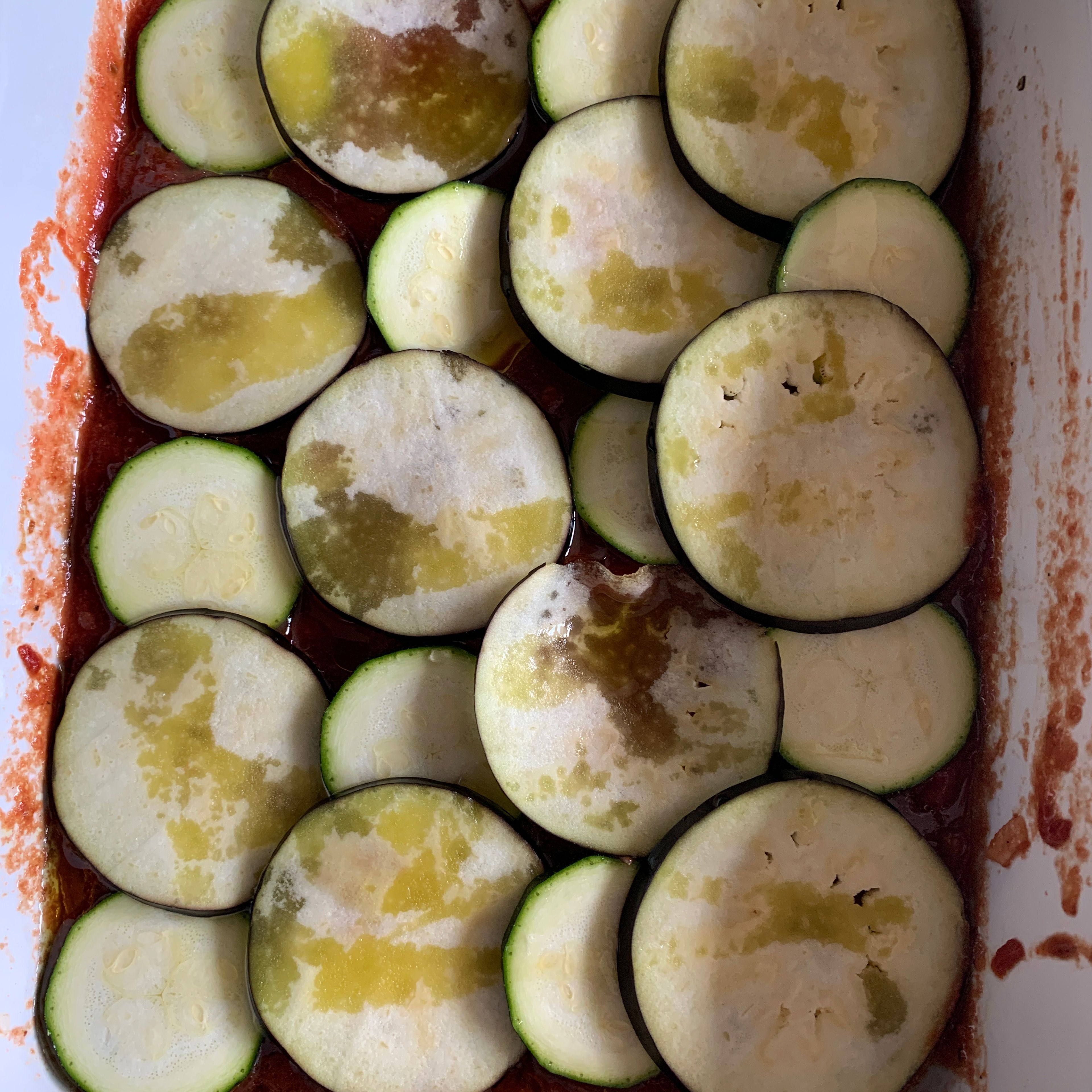 Die Aubergine und die Zucchini in dünne Scheiben schneiden auf der Tomatensauce schichten. Alles mit 2 EL Olivenöl beträufeln und im Ofen bei 180 Grad Umluft 45 Min schmoren.