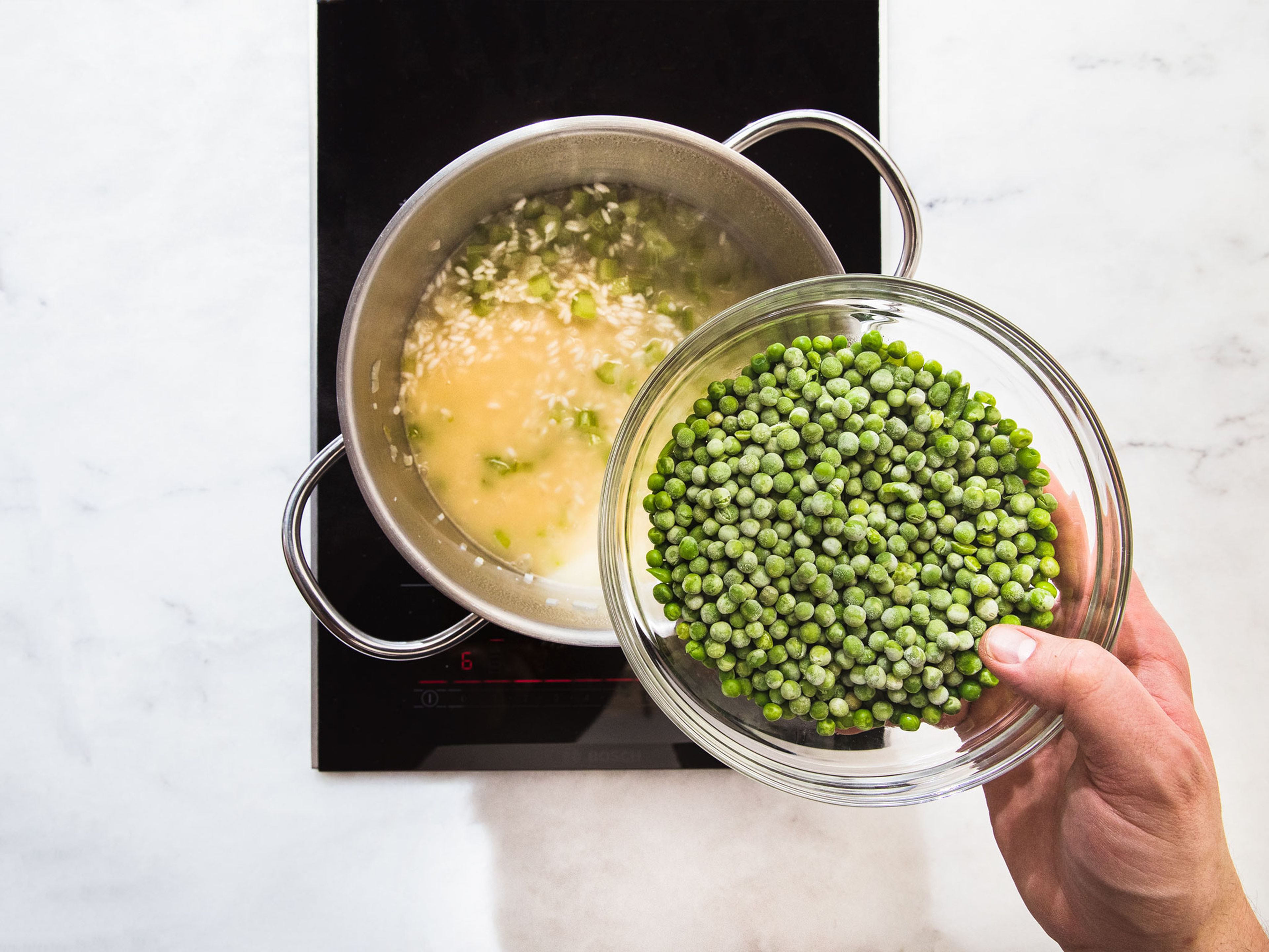 Melt butter in a large pot over medium heat and sauté minced onion, garlic, and celery for approx. 2 – 3 min., or until fragrant. Add rice and fry over low heat for approx. 5 min. Deglaze with the wine and some warm vegetable broth. Stir until the liquid is absorbed and add peas.