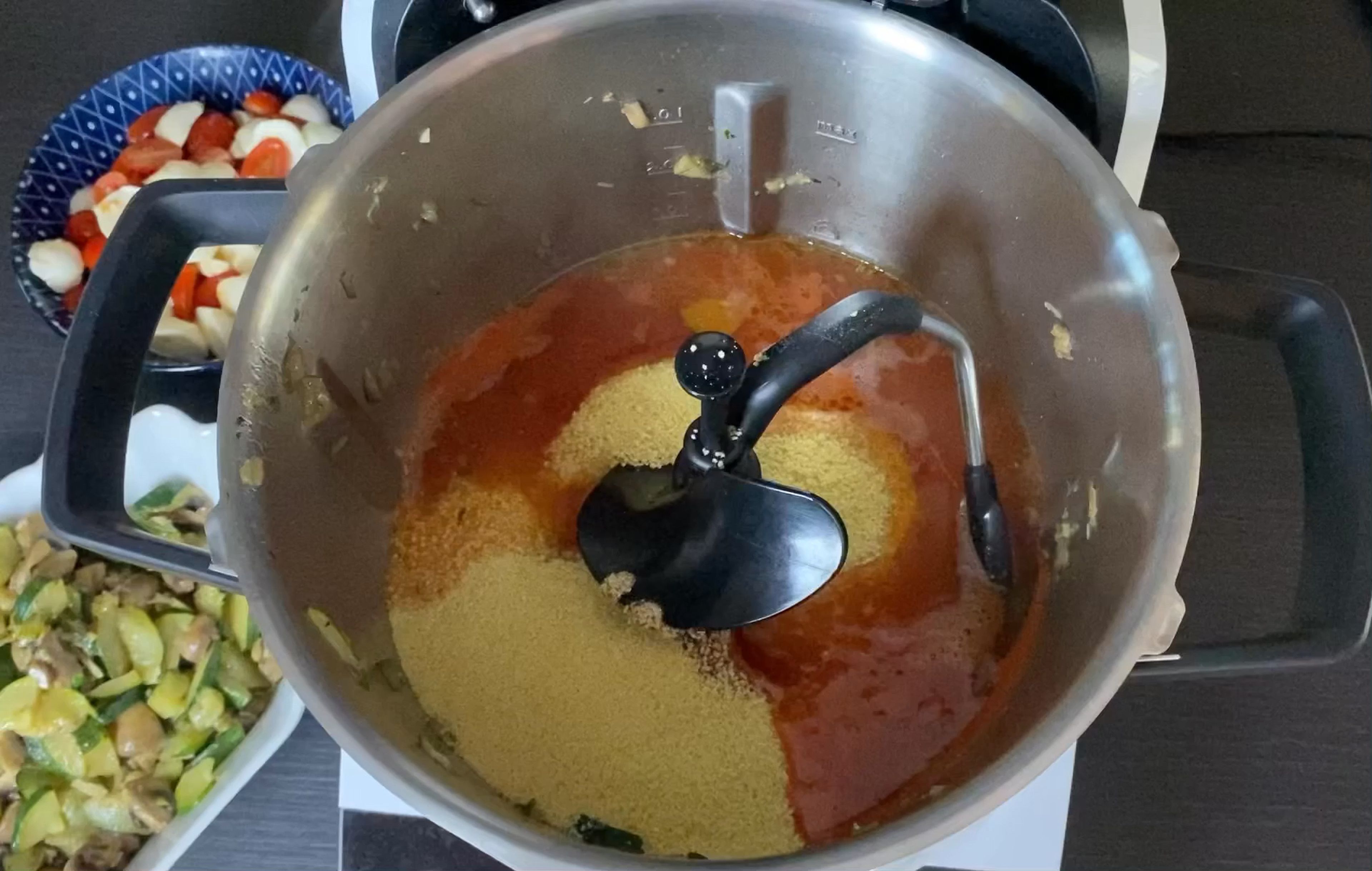 Jetzt geht es an den Couscous. Der benötigt heißes Wasser, also das Wasser mit dem Tomatenmark im Automatikprogramm "Wasser schnell aufheizen“ bei geschlossenem Deckel und eingesetztem Messbecher zum Kochen bringen. Wenn das Wasser heiß ist, den 3D-Rührer vorsichtig einsetzen. Nun kommen Couscous, Salz und Pfeffer dazu. Die Zutaten werden bei geschlossenem Deckel mit eingesetztem Messbecher schnell untergerührt (3D-Rührer | Stufe 6 | 1 Min.) und ruhen abschließend für 5 Min.