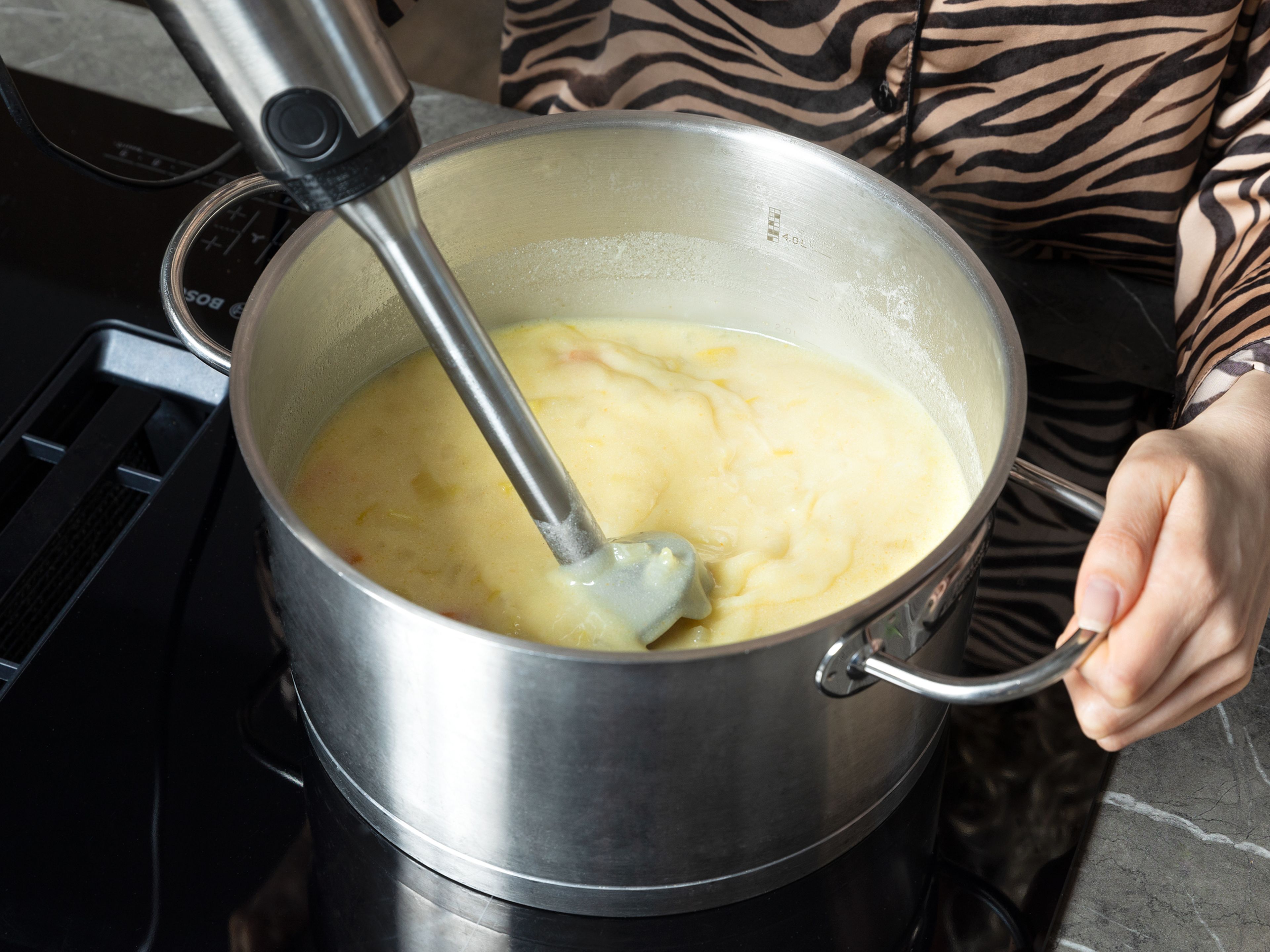 Den größten Teil der Crème fraîche unter die Suppe rühren, einen Klecks zum Servieren aufheben. Die Suppe im Topf mit einem Stabmixer kurz anpürieren, bis sie cremig, aber noch stückig ist. Die Hitze wieder auf mittlere Stufe stellen.