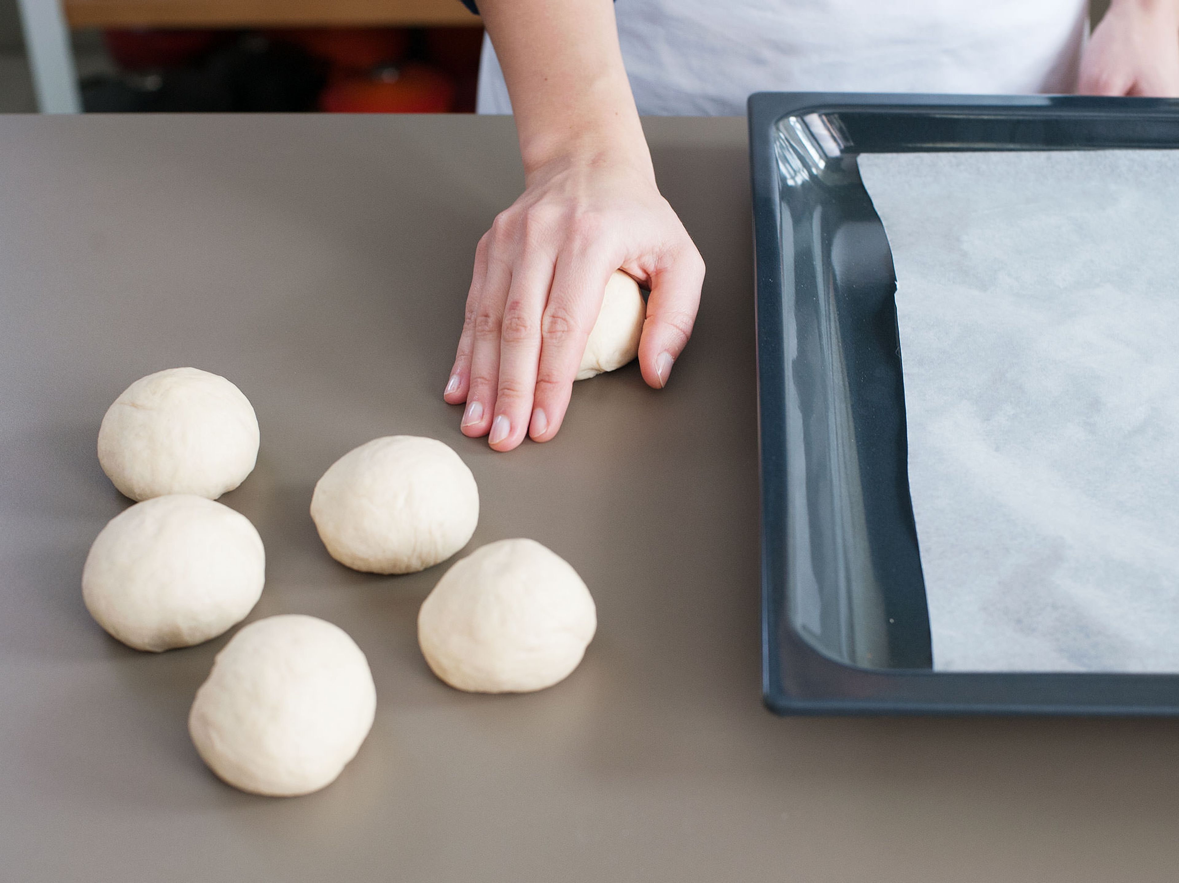Then, roll dough pieces into smooth balls, transfer back to parchment-lined baking sheet, and cover with a damp kitchen towel. Let rise for another approx. 30 min. in a warm place.