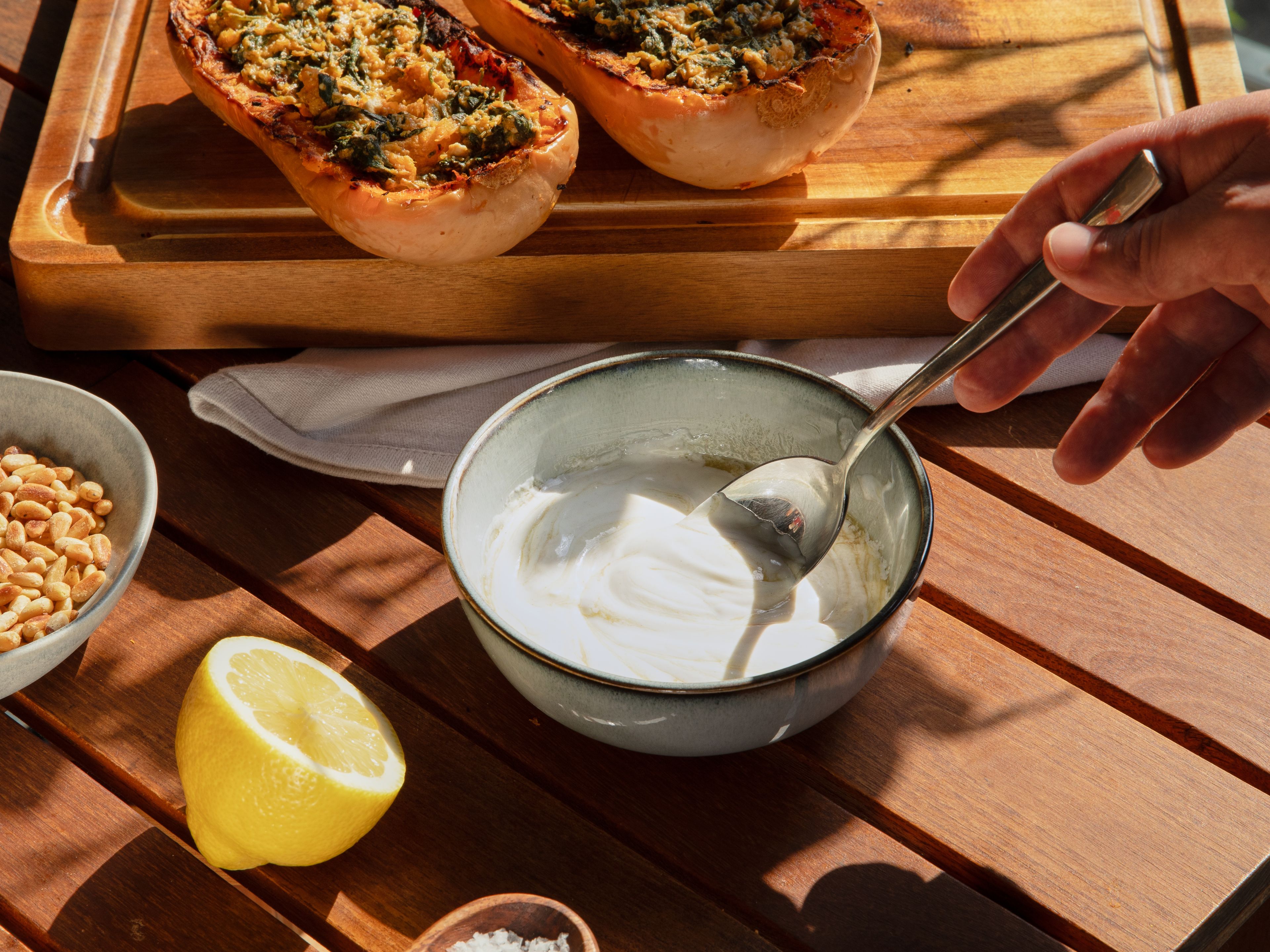 Für die Soße verbliebenen gehackten Knoblauch, griechischen Joghurt, Tahini, 1 EL Zitronensaft, restliches Olivenöl, Salz und Pfeffer cremig verrühren. Die gefüllten Butternut-Kürbisse mit der Joghurt-Tahini-Soße anrichten und mit den gerösteten Pinienkernen und nach Belieben ein paar Thymianblättern und Chilliflocken bestreuen.