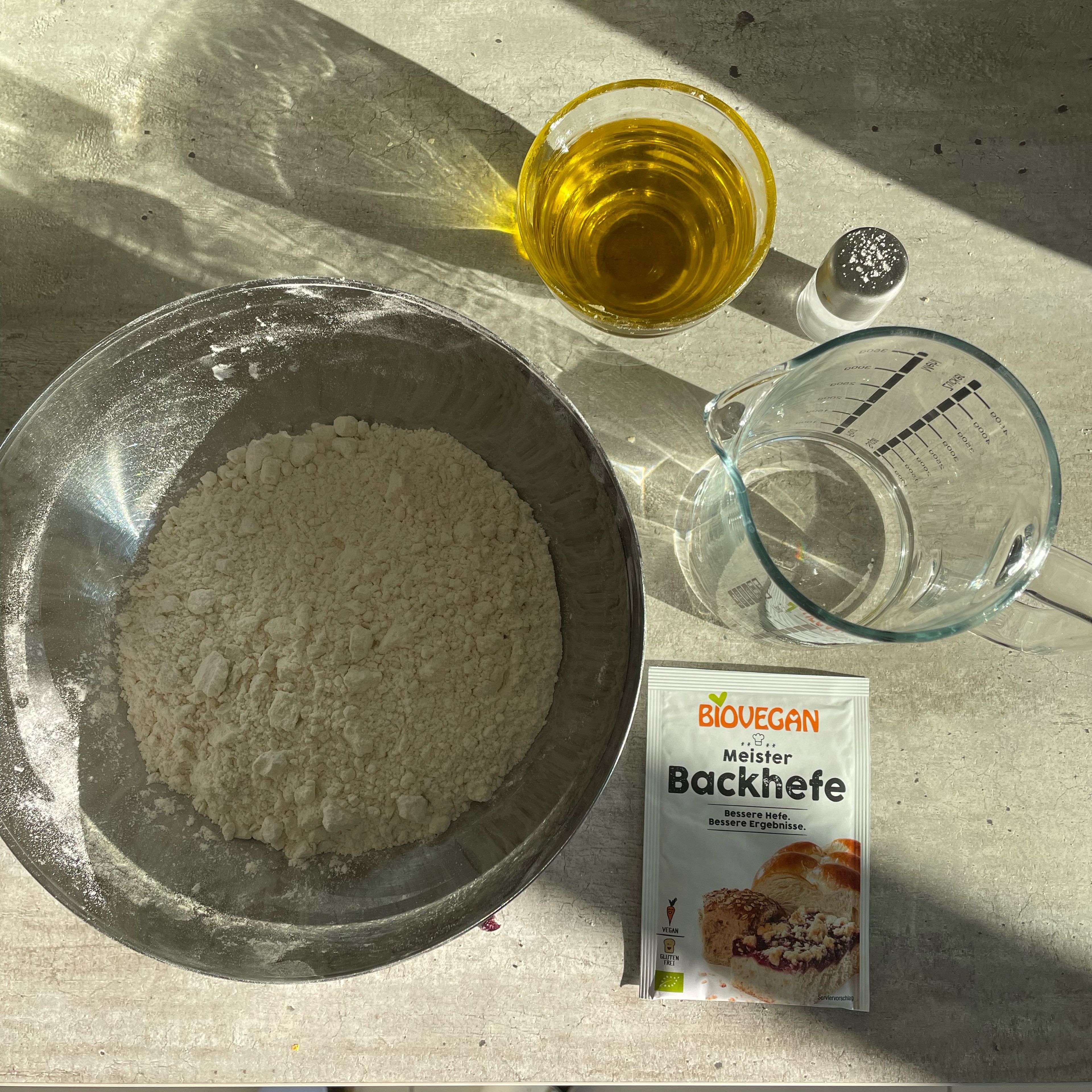 In the meantime we can prepare the dough. Add the flour, yeast and salt to a bowl. Mix the water and oil in a different bowl - then start adding the flour mix, little by little while mixing all ingredients.