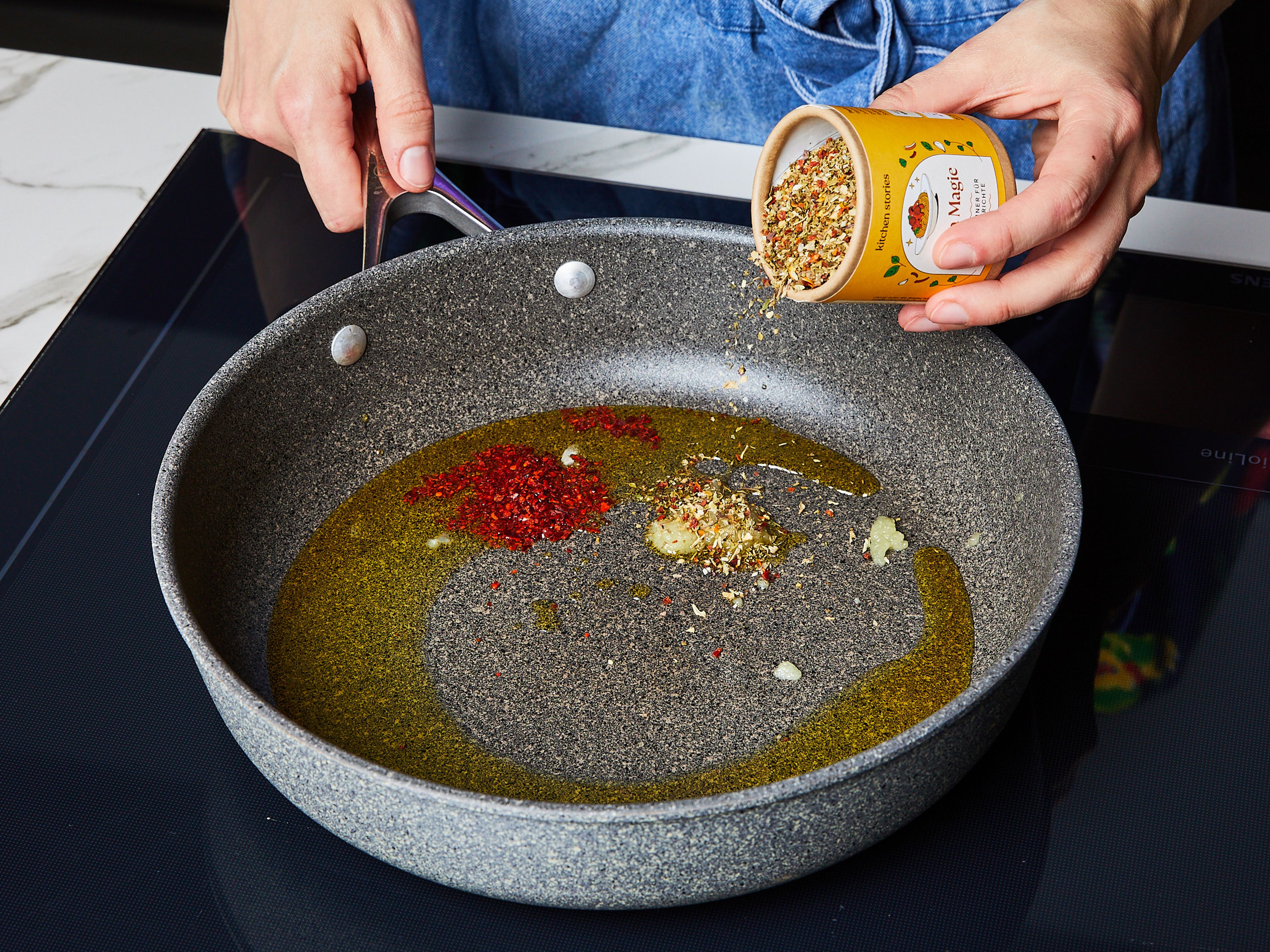 Für die Tomatenbrühe Wasser zum Kochen bringen, Tomatenmark hinzufügen und verrühren. Mit Salz und Pfeffer würzen und bei schwacher Hitze warm halten. Knoblauch schälen und fein reiben. In einer großen beschichteten Pfanne Olivenöl bei mittlerer bis hoher Temperatur erhitzen, Knoblauch, Chiliflocken und Pasta Magie Gewürzmischung hinzufügen. Alles gut vermengen.