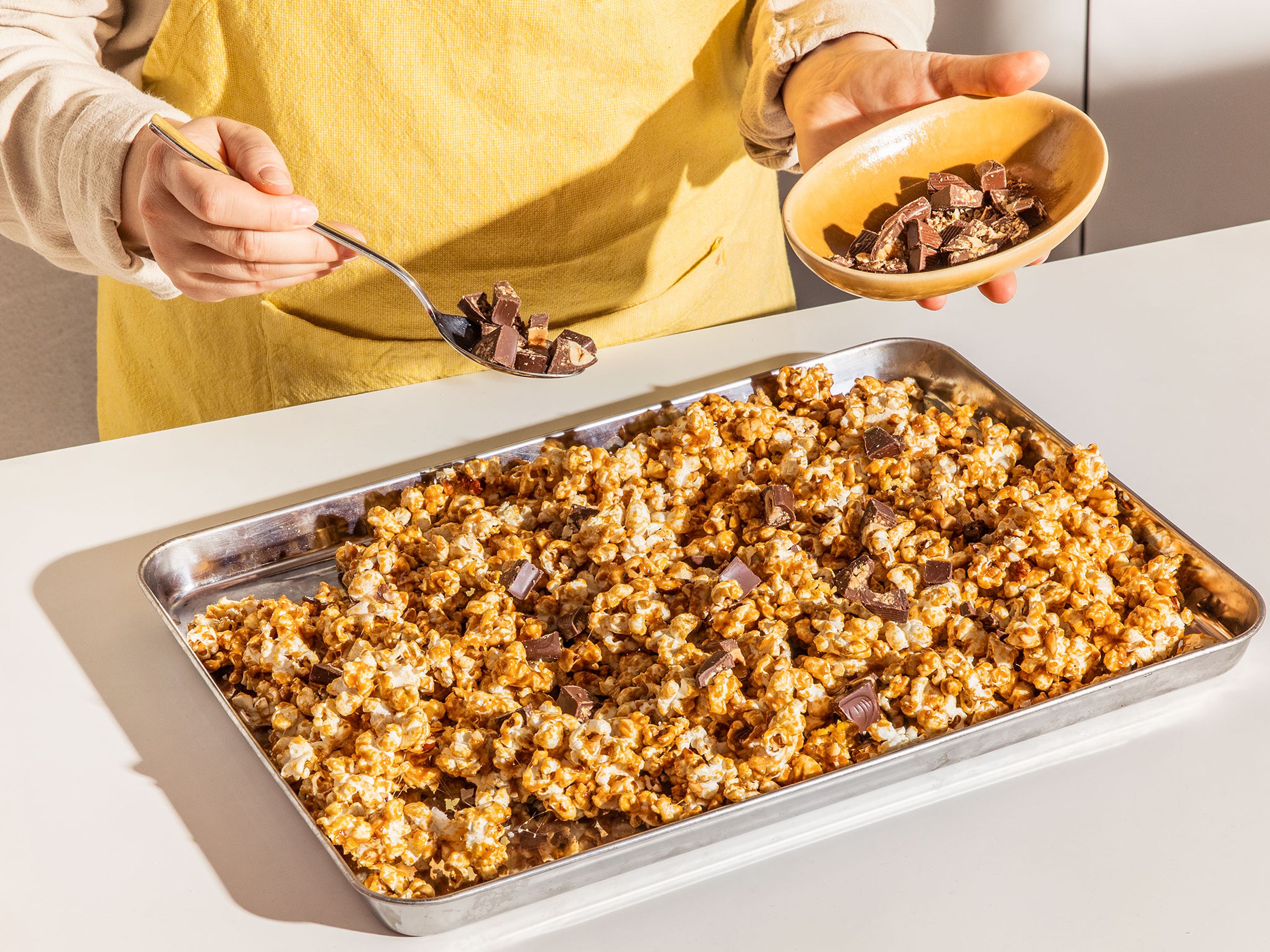 Die Ferrero Küsschen Stücke auf dem noch warmen Karamell-Popcorn verteilen, sodass sie leicht schmelzen. Mit grobem Meersalz bestreuen. Das Popcorn komplett auskühlen lassen. Danach grob zerbrechen.