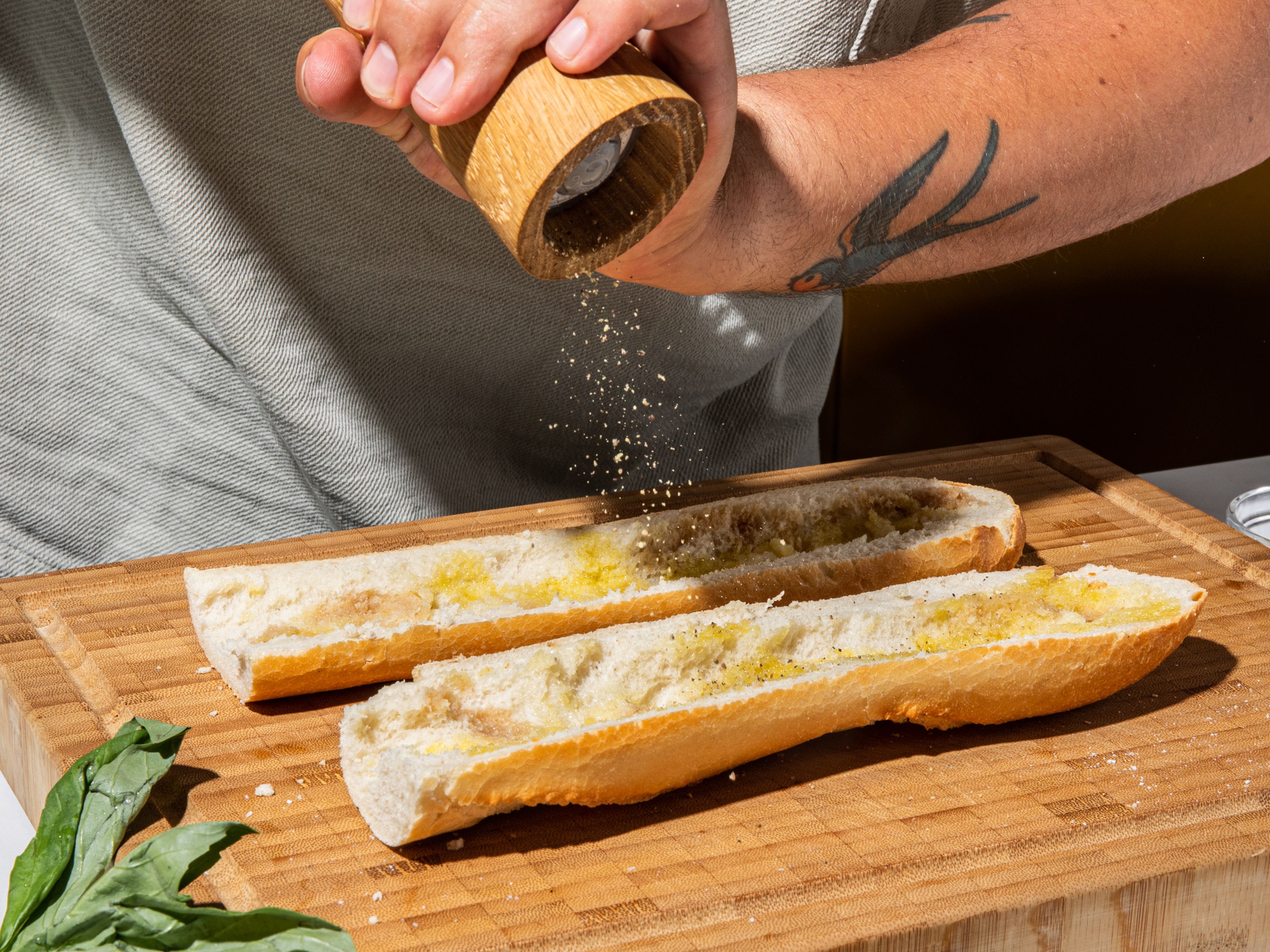Das Baguette der Länge nach aufschneiden und etwas von der weichen Krume an der Ober- und Unterseite des Brotes entfernen, um Platz für die Füllungen zu schaffen. Mit Olivenöl und Essig beträufeln und mit Salz und Pfeffer bestreuen.