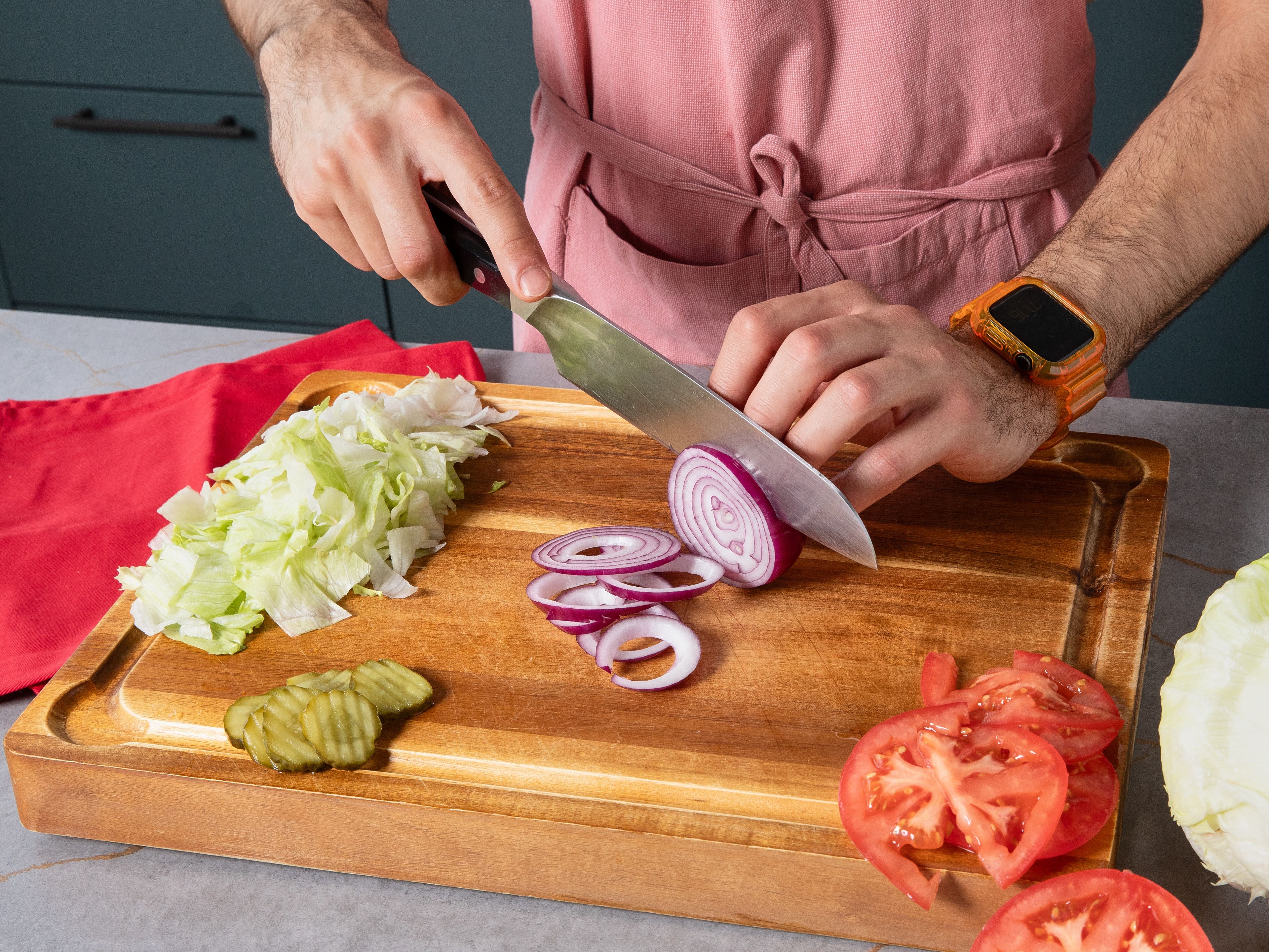 Für die Big Mac Bowl zuerst Eisbergsalat waschen und klein schneiden, Tomaten in dünne Scheiben halbieren. Rote Zwiebel in feine Ringe schneiden. Eisbergsalat, Tomaten, Burgergurken und Zwiebelringe in eine große Schüssel geben und alles gut vermengen.