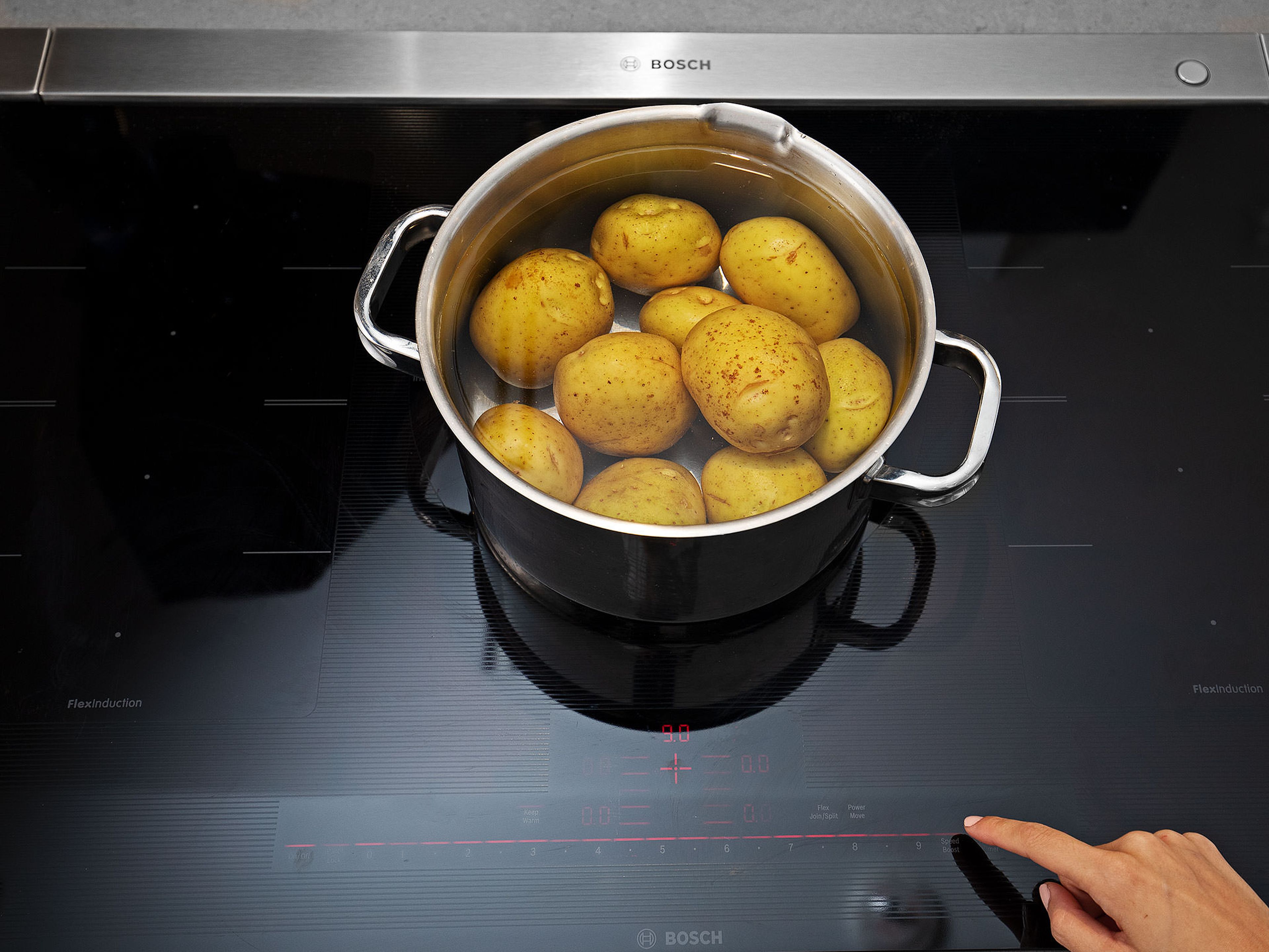 Knoblauchzehen schälen und zerdrücken. Kartoffeln putzen und in einen großen Topf mit kaltem Wasser und der Hälfte der Knoblauchzehen legen. Wasser großzügig salzen und zum Kochen bringen. Kartoffeln in etwa 30 - 35 Min. gar kochen. Abgießen und beiseitestellen.