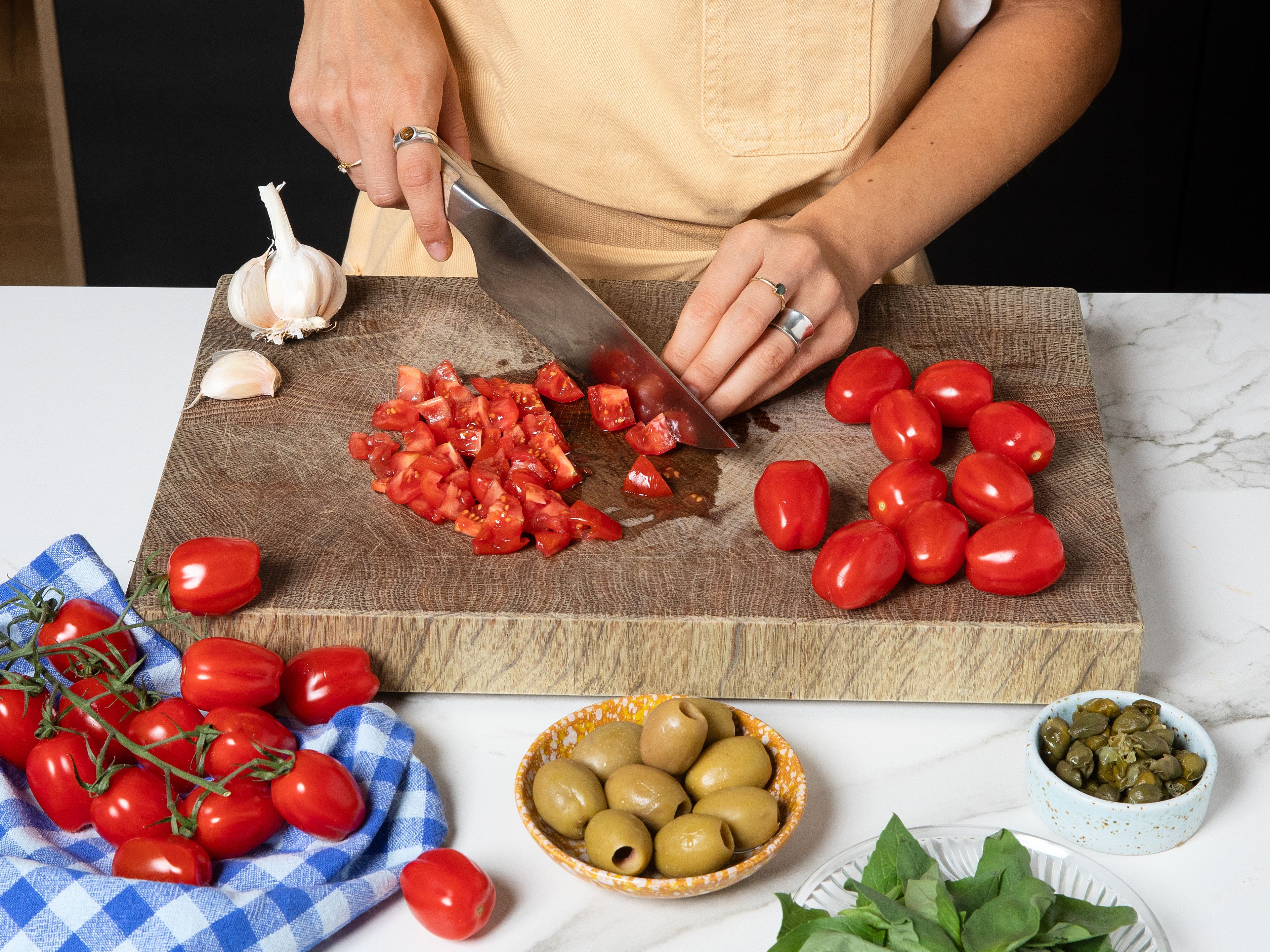 Cut the tomatoes into small cubes. Cut the olives into similarly sized pieces. Roughly chop the capers and finely chop or grate the garlic. Add everything to a large bowl and drizzle with olive oil. Season with salt and pepper (be careful with the salt at first, as the olives and capers already bring plenty of seasoning). Add half of the basil and mix well. Let the sauce sit while the pasta cooks.