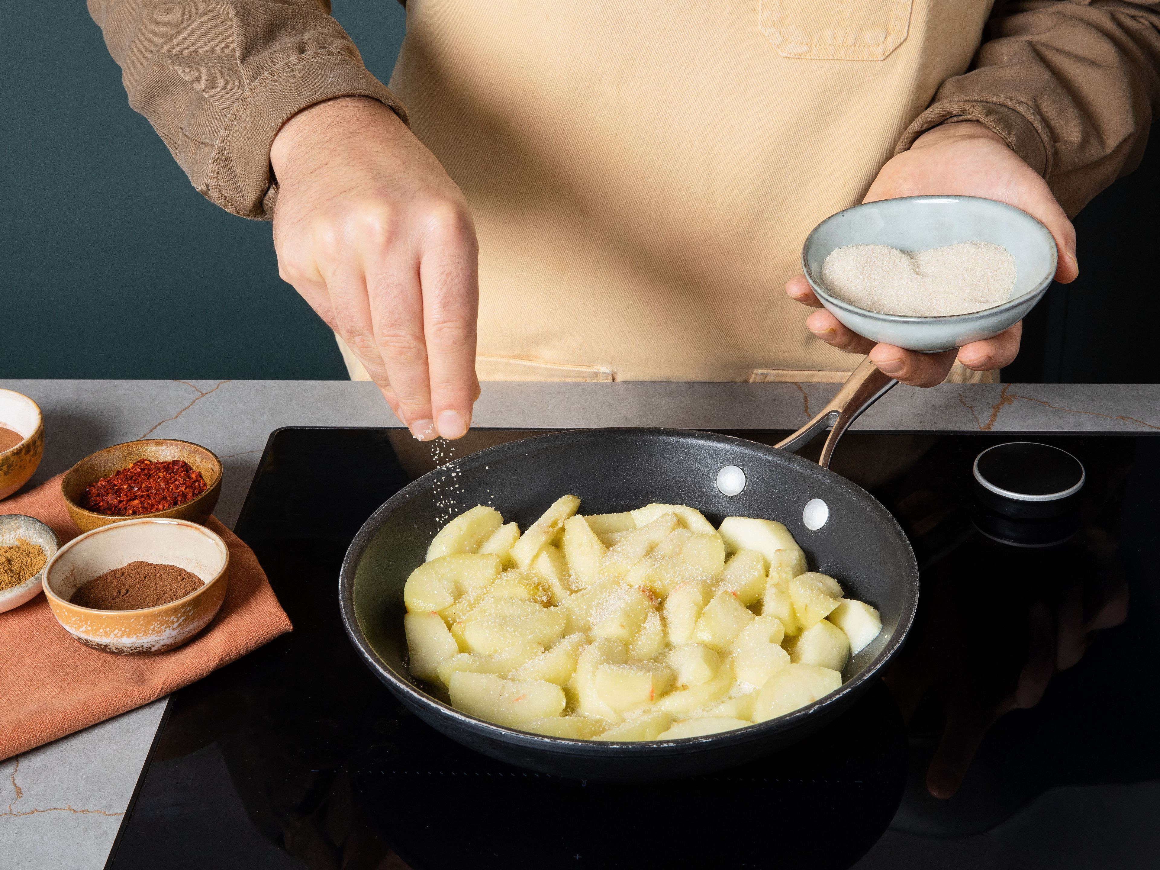 Für die Gewürzäpfel die Äpfel schälen, entkernen und in Spalten schneiden. In einer Pfanne die restliche Butter erhitzen, die Äpfel hinzugeben und darin kurz anschwitzen. Mit Zucker, Zimt, Kreuzkümmel, Chili und Nelken bestreuen, umrühren und leicht karamellisieren lassen, bis ein Sirup entsteht. Wasser mit Speisestärke verrühren, zu den Äpfeln geben und kurz aufkochen, bis die Soße eindickt. Zum Servieren Gulasch auf Tellern anrichten und mit den Salbeikartoffeln und Gewürzäpfeln servieren.