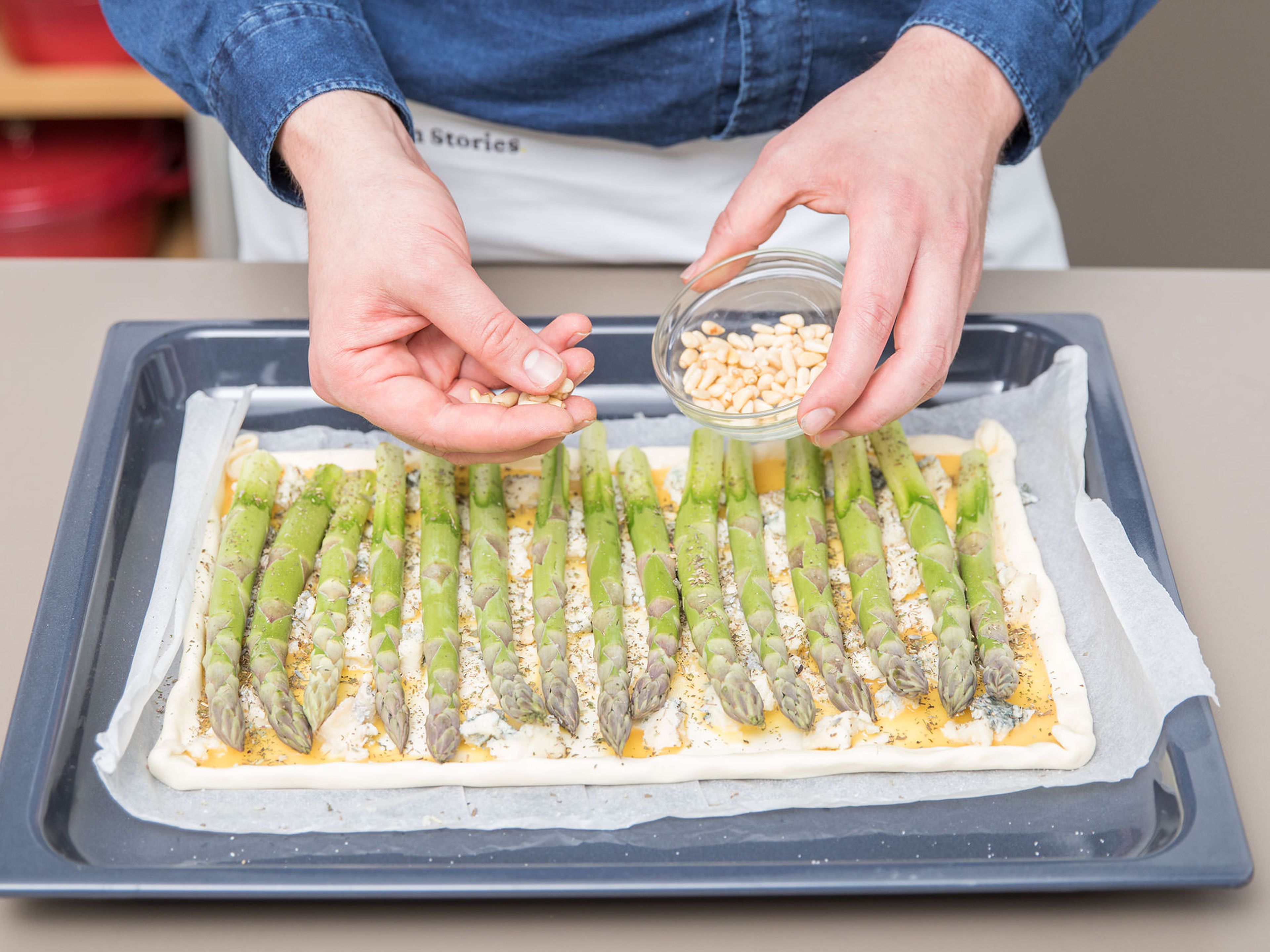 Prepare the asparagus and chop the garlic. Arrange the asparagus on top of the egg layer, then add pine nuts, garlic, herbes de Provence, salt, and pepper. Bake at 180°C/360°F for approx. 20 min. until golden. Enjoy!
