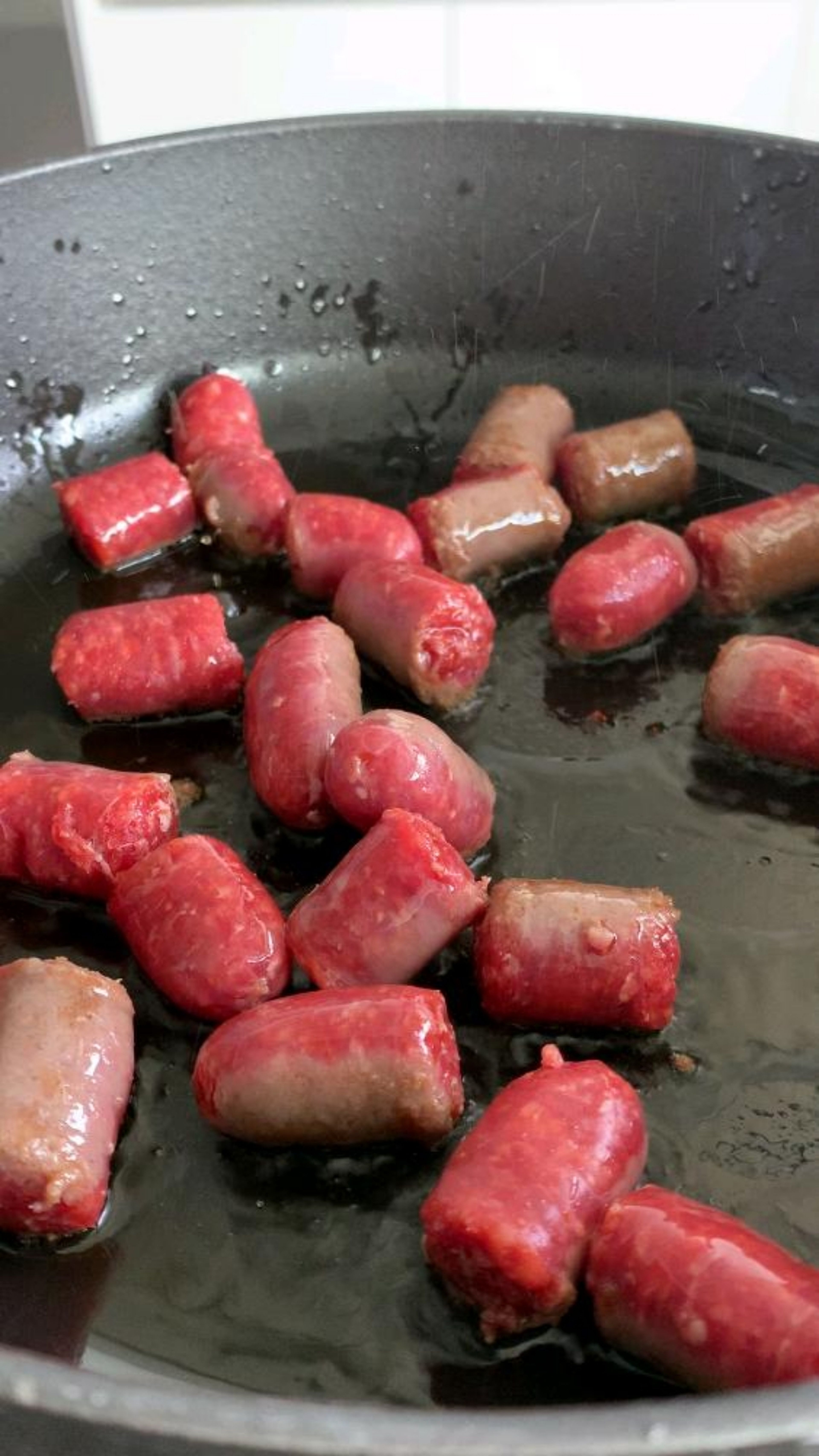 Die Würstchen in der Pfanne mit Olivenöl scharf anbraten. Danach die Zwiebel und den Knoblauch dazugeben.