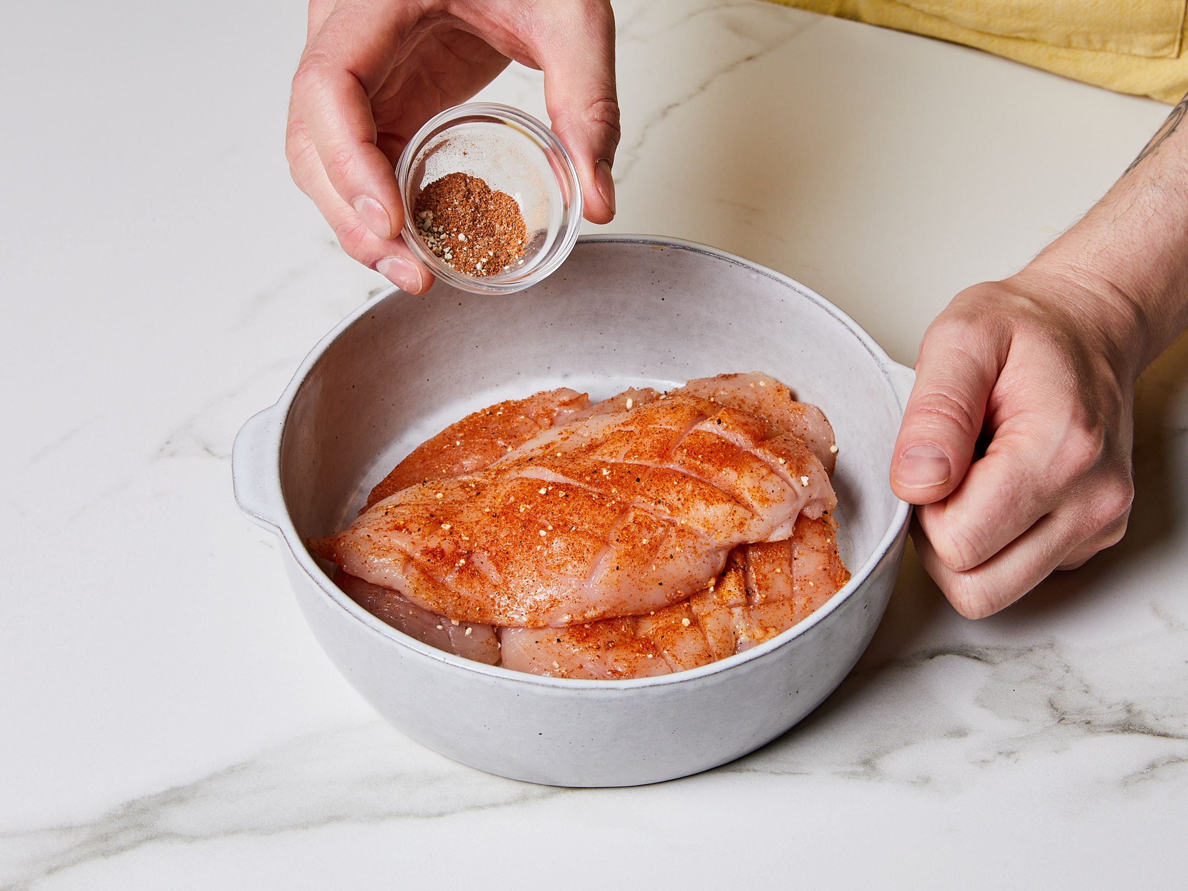 Hähnchenbrüste horizontal in zwei Filets pro Brust schneiden. Die Oberfläche der Filets rautenförmig einritzen, um die Oberfläche zu vergrößern, den Geschmack zu verbessern und die Garzeit zu verkürzen. Filets in einer Schüssel mit Paprikapulver, Knoblauchpulver, Zwiebelpulver und Salz würzen.