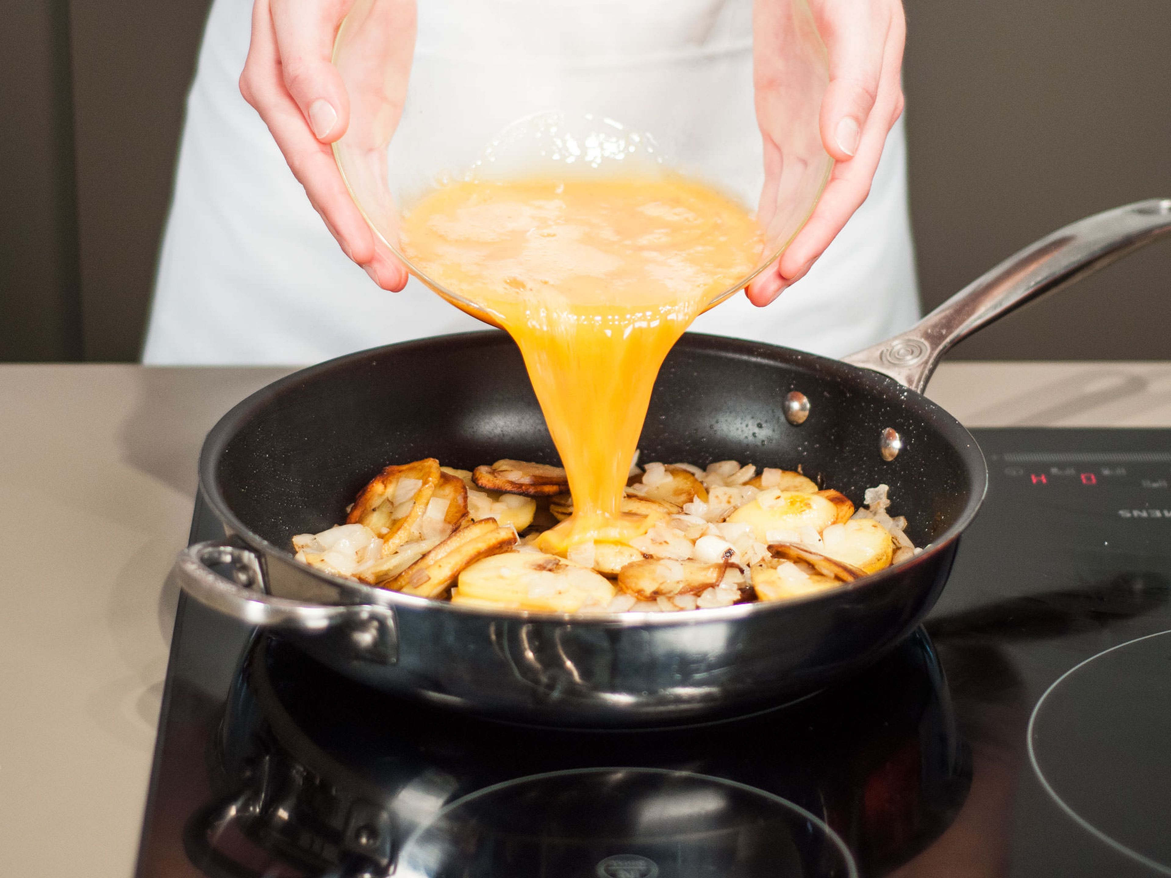 Kartoffeln mit Eiern begießen und bei geringer Hitze ca. 8 – 10 Min. anbraten, bis die Unterseite und die Ränder anfangen zu stocken. Dann mit einem Holzspatel am Rand entlang fahren. Große Servierplatte oder einen Teller obenauf legen. Mit einer Hand die Platte und mit der anderen Hand den Griff der Pfanne festhalten. Nun die Tortilla schnell auf die Servierplatte überführen und mit der rohen Seite nach unten zurück in die Pfanne gleiten lassen. Von der anderen Seite ca. 4 – 5 Min. anbraten, bis das Ei vollkommen gestockt ist. Alternativ die Pfanne bei 200°C in den Backofen schieben und ca. 10 Min. fertig backen. Auf einer Servierplatte anrichten und in Stücke schneiden.