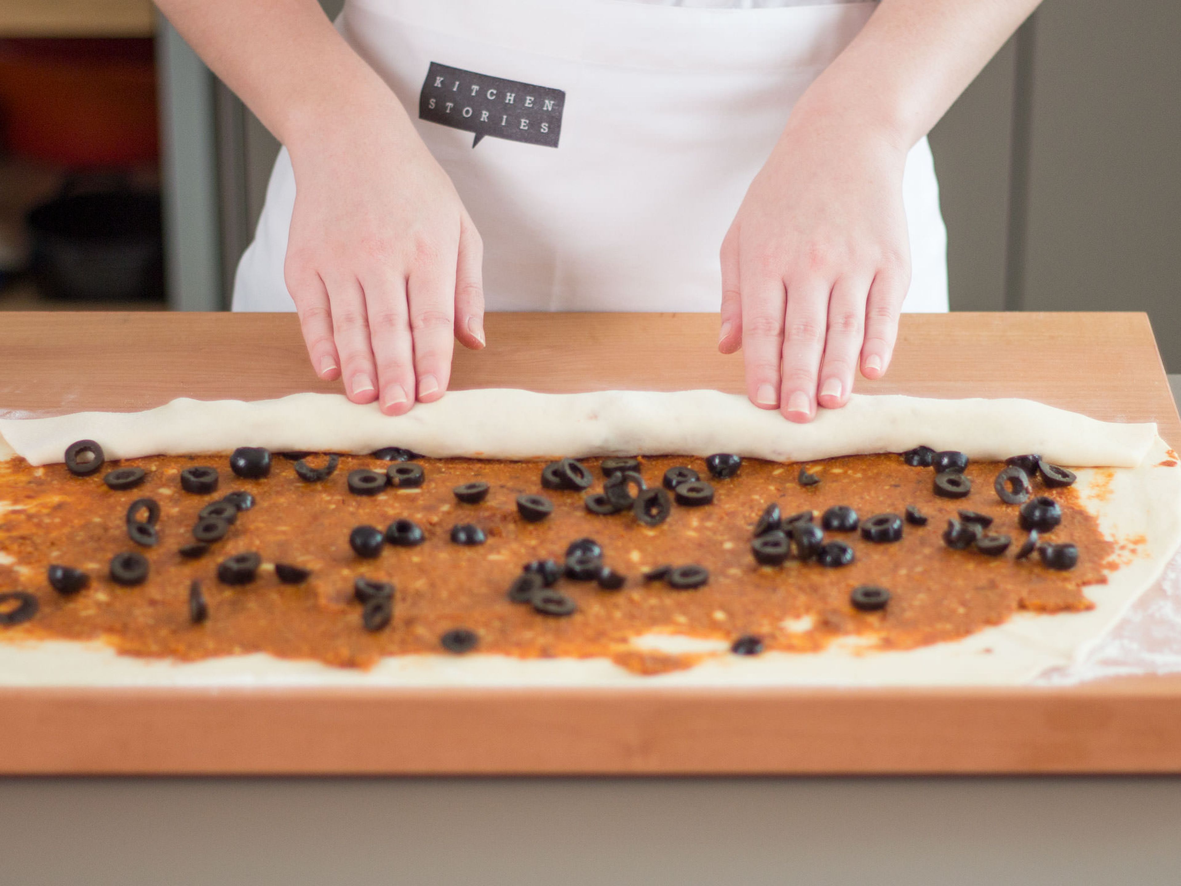 On a lightly floured work surface, flatten out dough with a rolling pin into a large rectangle. Evenly spread sun dried tomato paste over dough and sprinkle olives on top. Then, roll dough from side to side to form a long log.