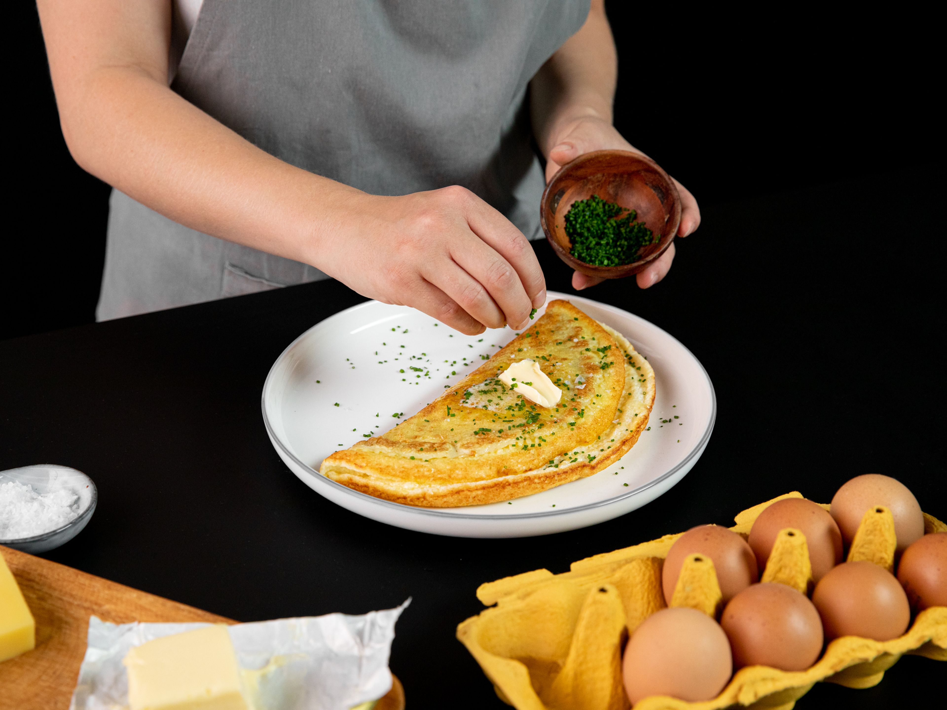 Deckel von der Pfanne nehmen und restlichen Käse auf das Omelett reiben. Der Boden des Omelettes sollte goldbraun und die Oberfläche gerade so gegart sein.  Das Omelett umklappen und auf einen Servierteller geben. Mit gehacktem Schnittlauch bestreuen und mit Brot und Salat servieren. Guten Appetit!
