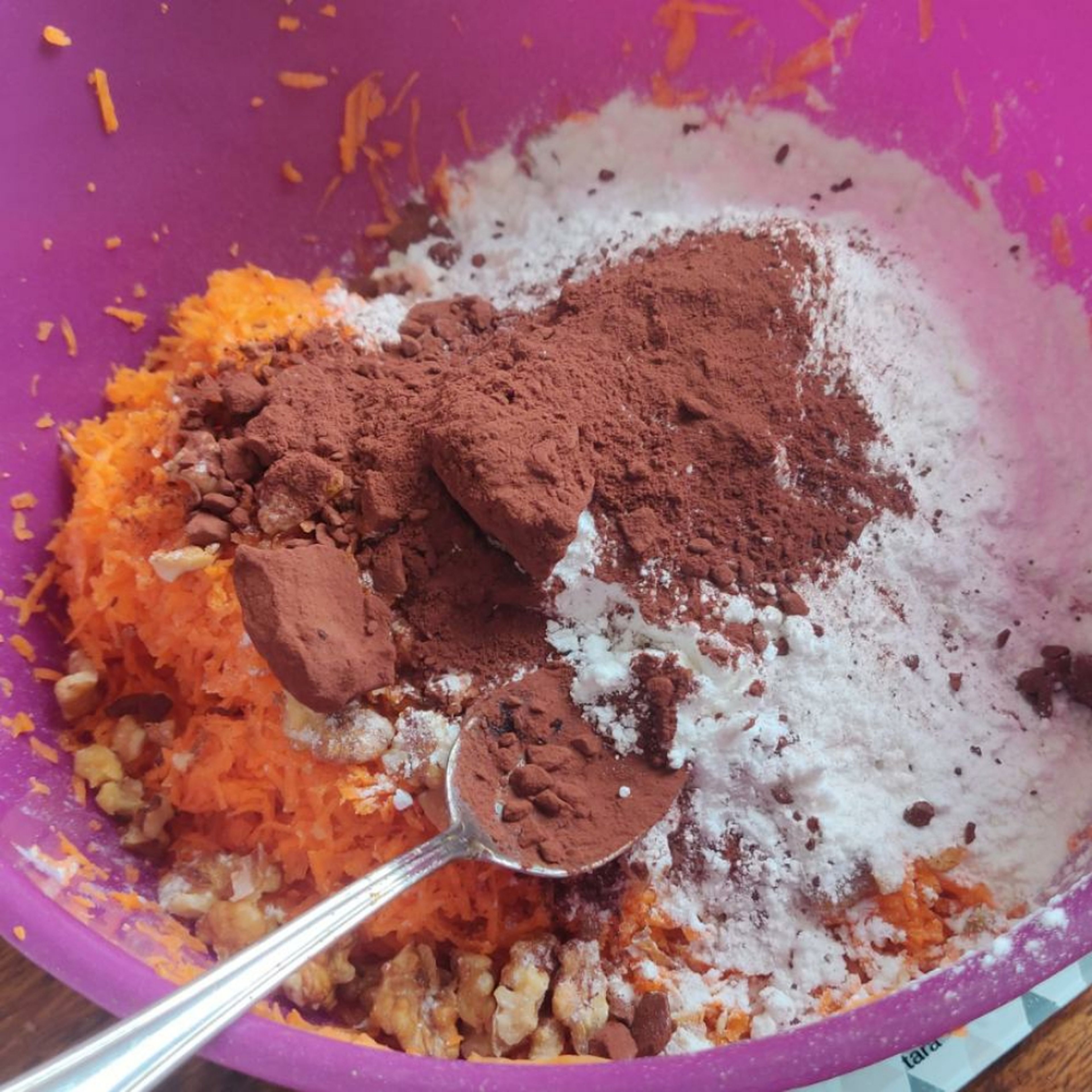 Zu dem bisherigen Mix geriebene Karotten und Äpfel, Backpulver, Mehl, Kakao und zerkleinerte Nüsse geben.