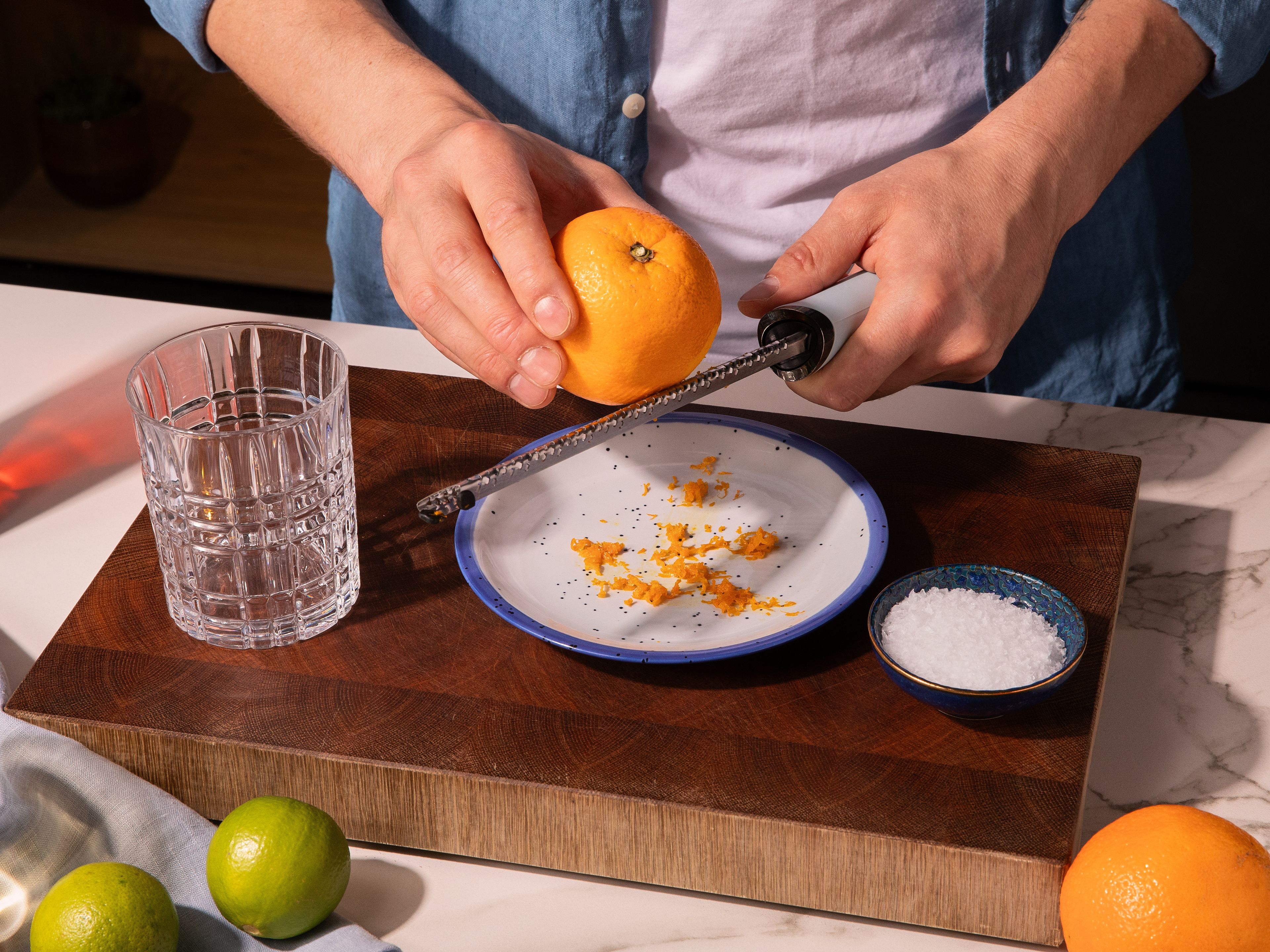Die Orange heiß abwaschen und etwas Schale fein abreiben. Orangenabrieb auf einem kleinen Teller mit Meersalz mischen. Den Rand eines Tumbler- oder Margarita-Glases mit einer Limettenspalte anfeuchten und im Salz-Orangen-Mix wenden. Die Limette und Orange auspressen. Eine Orangenscheibe für die spätere Garnitur aufheben.