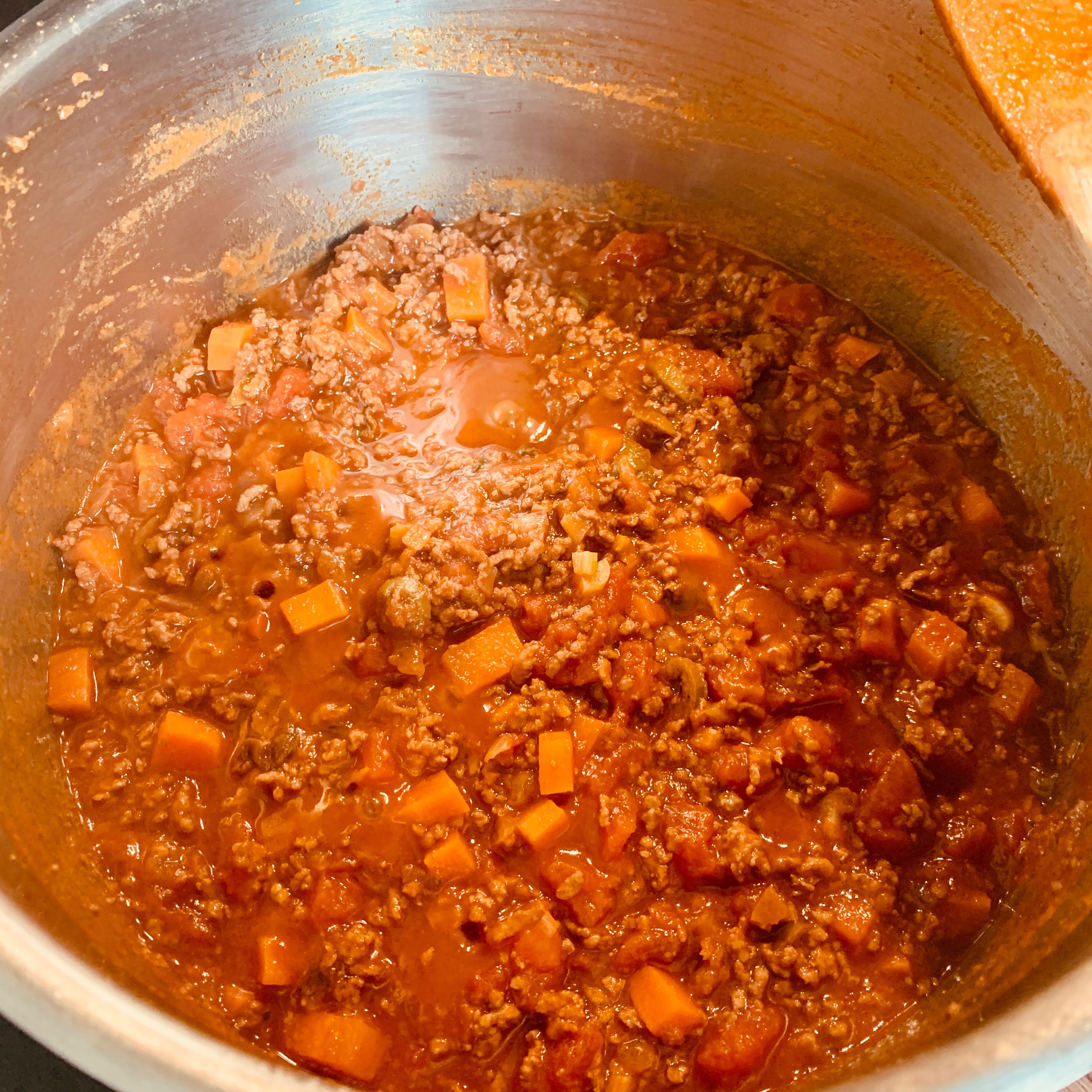 Karotten in Würfel, Knoblauch und Oliven klein schneiden und in den Topf dazu geben. Kurz mit anbraten und dann die Tomaten hinzu. Jetzt alles langsam bei leichter Hitze köcheln lassen. Ca. 45 min