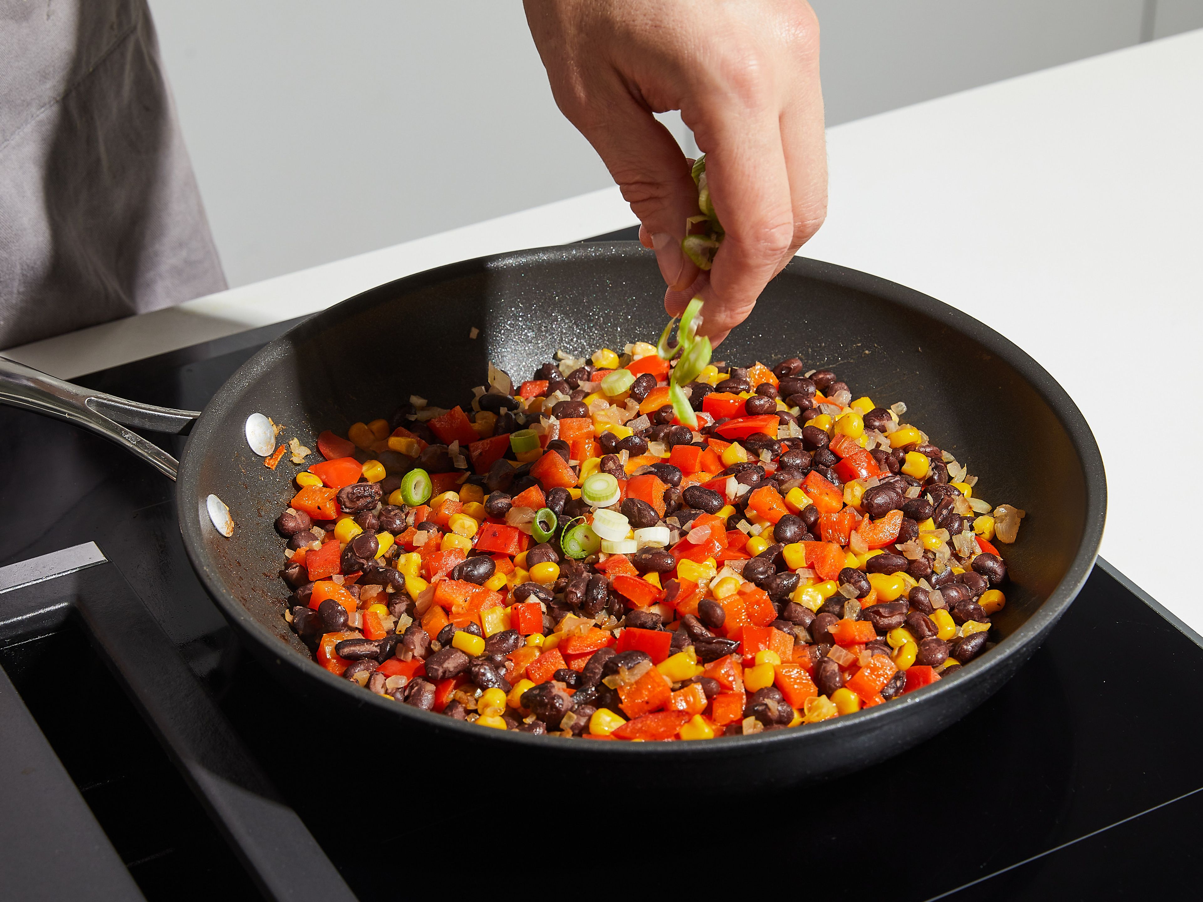 In a frying pan, heat some oil over medium heat. Fry onions approx. 1–2 min. until translucent, then add bell pepper, garlic, chili, black beans, and corn. Keep frying on medium heat for an additional 3–4 min., stirring occasionally until well combined. Remove from heat and add the white part of the chopped scallions.