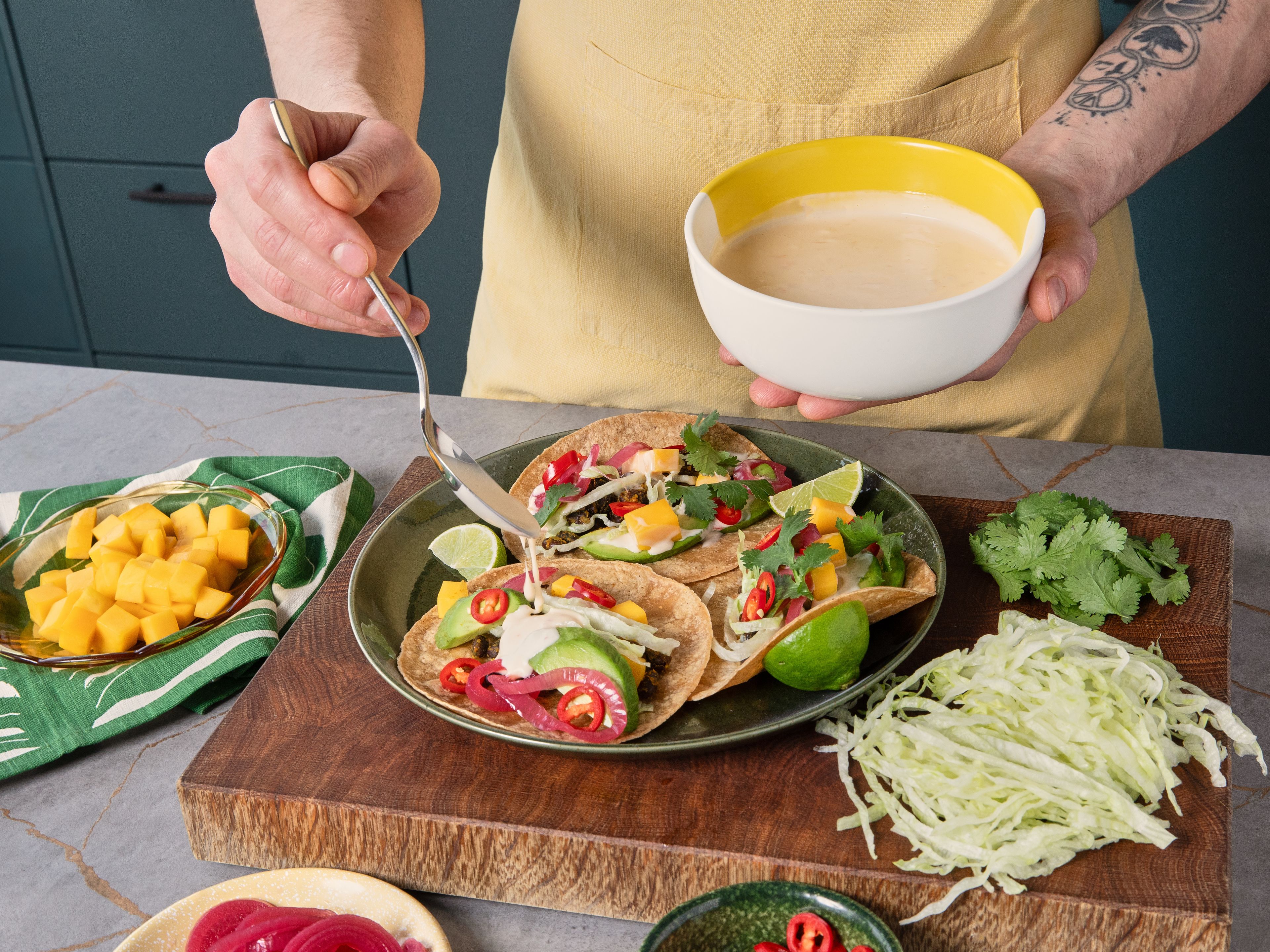 Die Mais-Tortillas in der zuvor verwendeten Pfanne kurz erwärmen. Danach mit Bohnen, Salat, Avocado, Mango-Würfeln, Mango-Chili-Mayo, eingelegten roten Zwiebeln, Chili und Koriander belegen und mit restlichen Limettenspalten servieren.