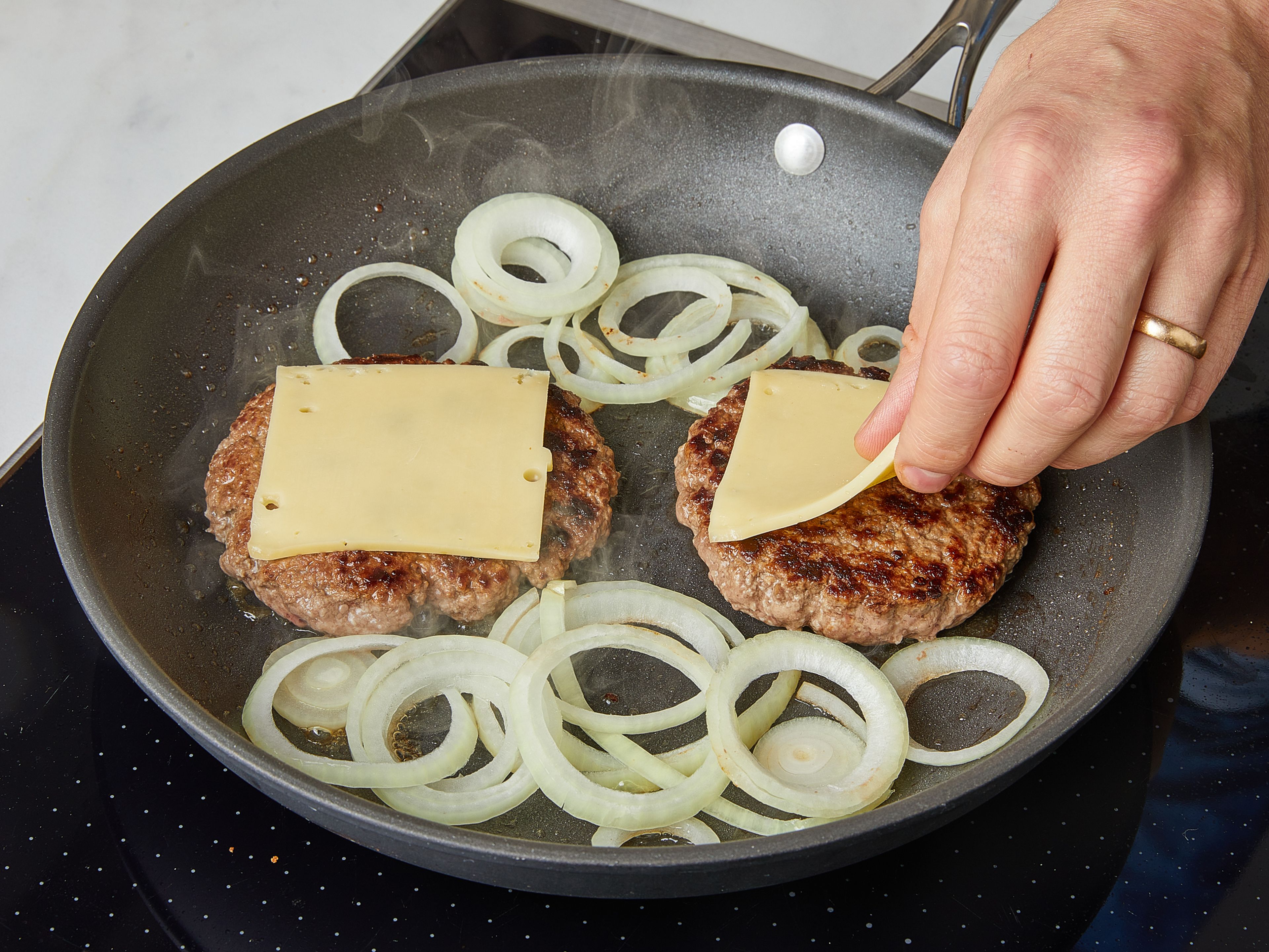 Cut the burger buns open and toast them in a large frying pan, cut-side down, for approx. 1–2 min. Remove the buns, and heat some oil in it. Add the patties and fry for approx. 4 min. on one side. Turn patties over and top with cheese. Add onion rings to the same pan, fry together with the patties for approx. another 4 min. Stir the onions occasionally.