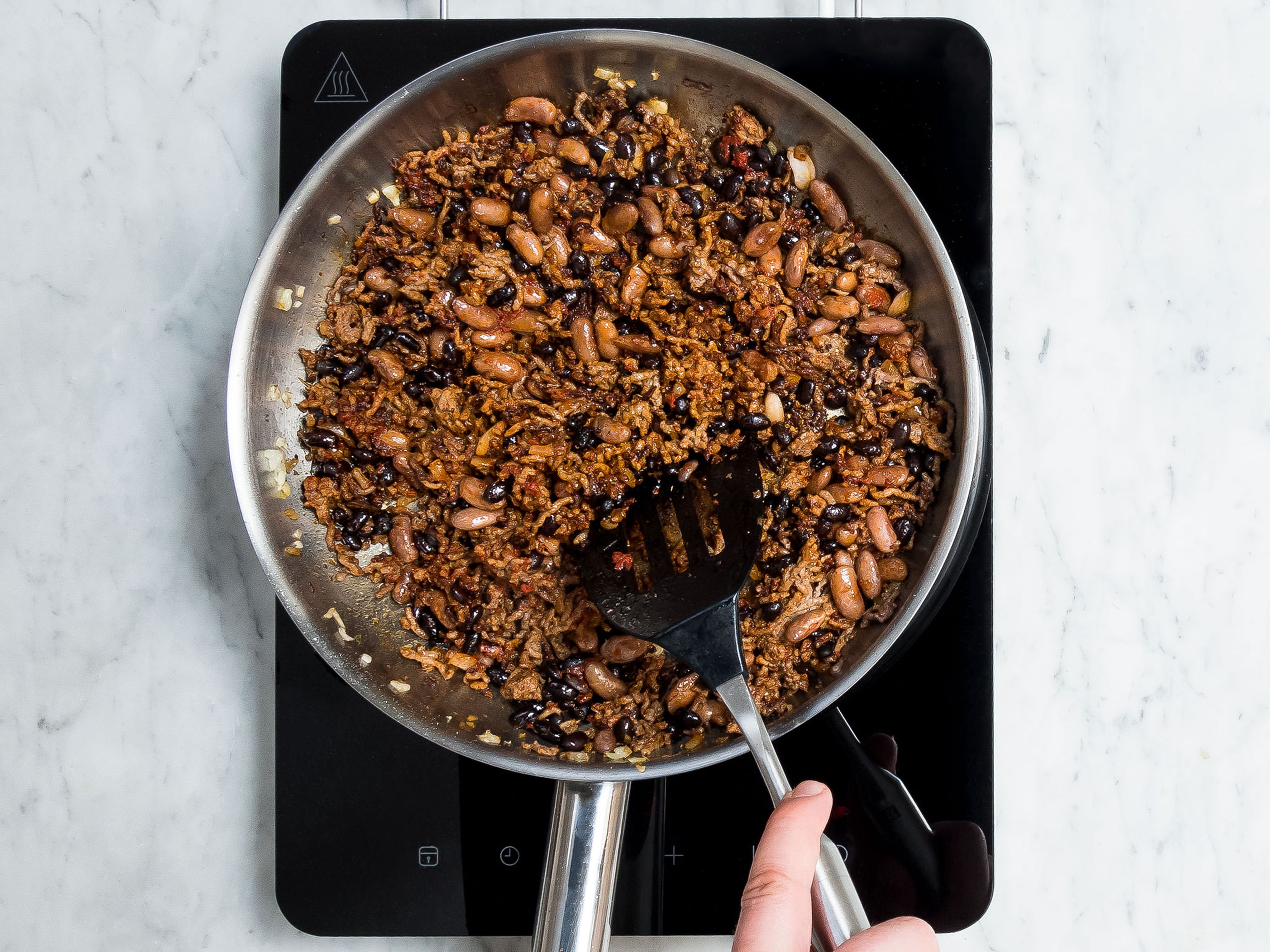 Preheat the oven to 180°C/370°F. Peel and dice onion. Drain and rinse canned beans. In a frying pan, heat olive oil and sauté diced onion. Add ground beef and fry for approx. 1 – 2 min. Add chili powder, paprika powder, ground cumin, Cayenne pepper, dried oregano, and sugar and season with pepper and salt. Mix well and fry for another 2 – 3 min. Stir in pinto beans, black beans, and tomato paste, then remove frying pan from heat.