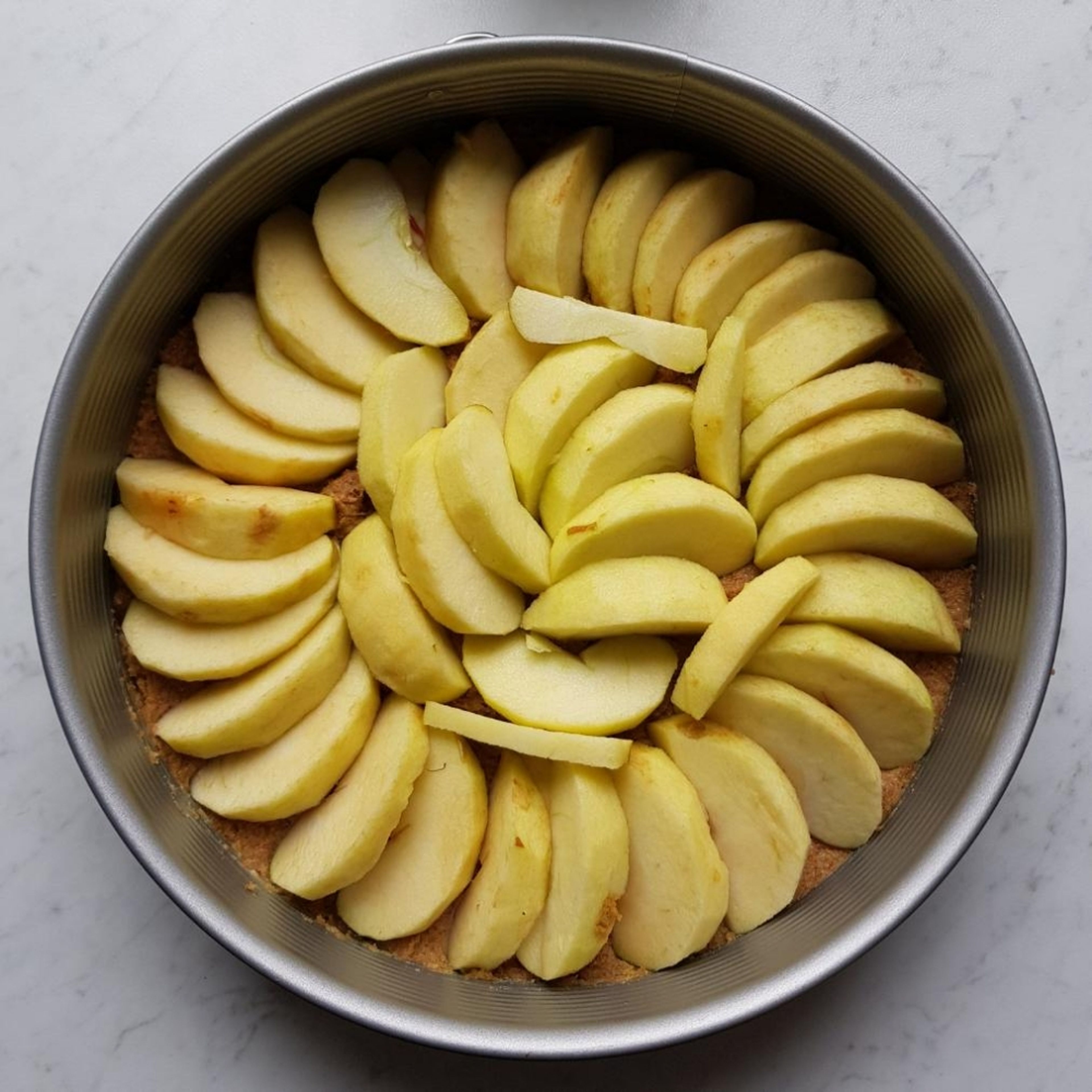 Die Äpfel schälen, entkernen und in Scheiben schneiden, die nun kreisförmig und großzügig auf dem Teig angeordnet bzw. leicht ineinander geschichtet werden. Je mehr Äpfel ihr unter bekommt, desto fruchtiger wird der Kuchen später.