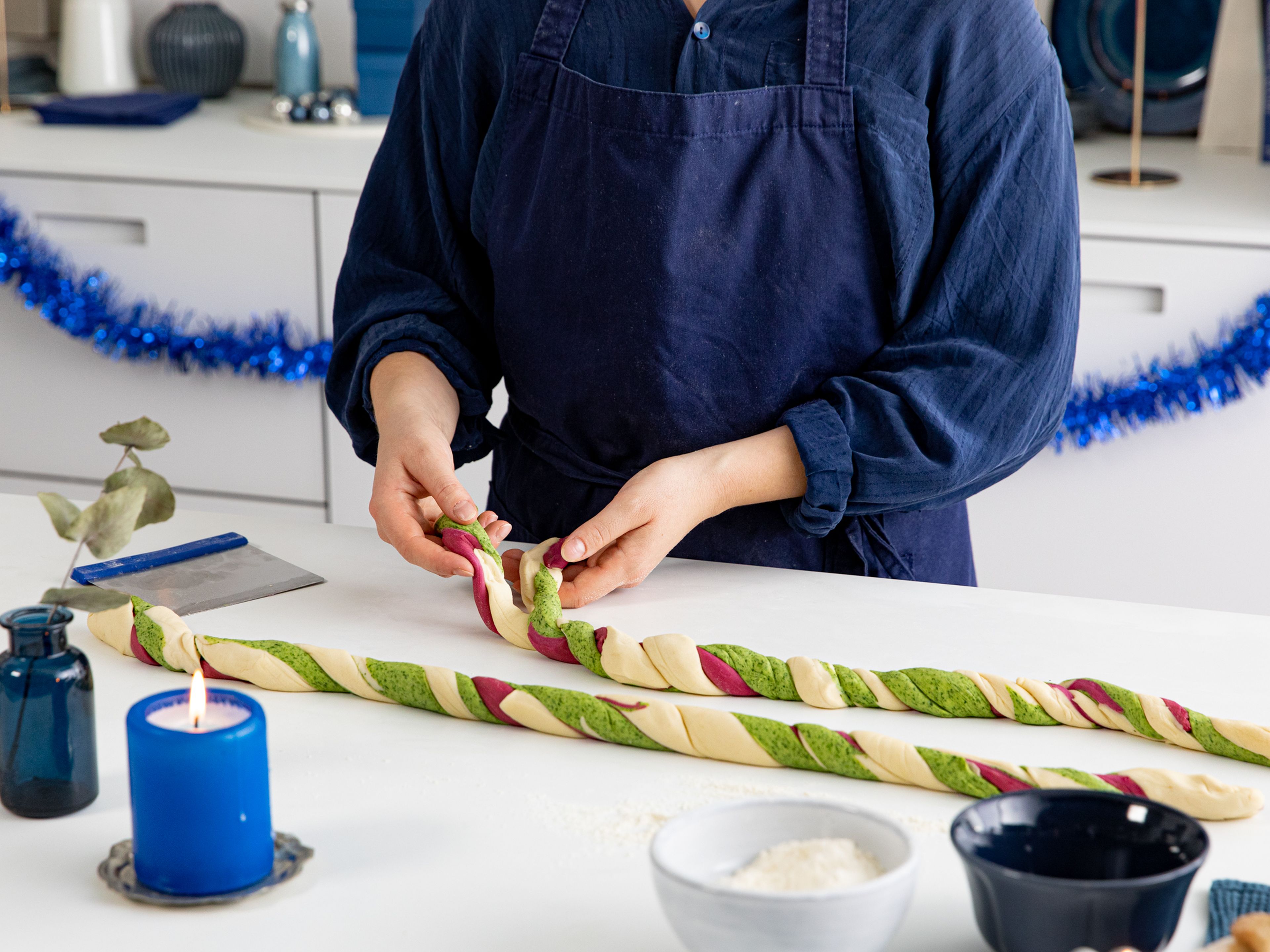 With damp hands and on a floured work surface, roll each dough ball into a thin log. Carefully wrap the colored strands around the plain one, then halve the roll with a knife lengthwise and weave the two parts together. Squeeze and roll to combine.