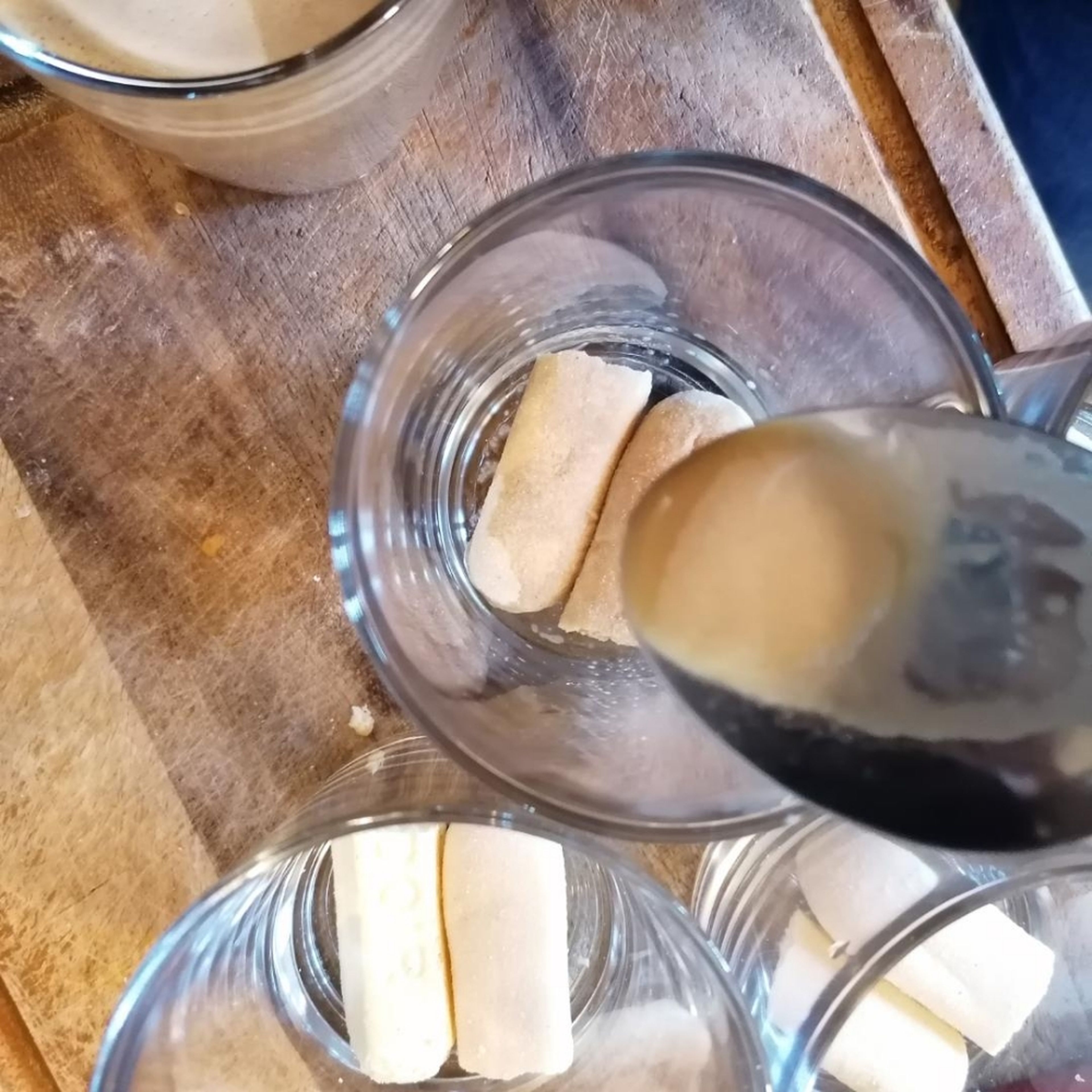 Die erste Lage Löffelnbiskuits in die Gläser verteilen und mit je einem EL Espresso-Milch-Mischung tränken.