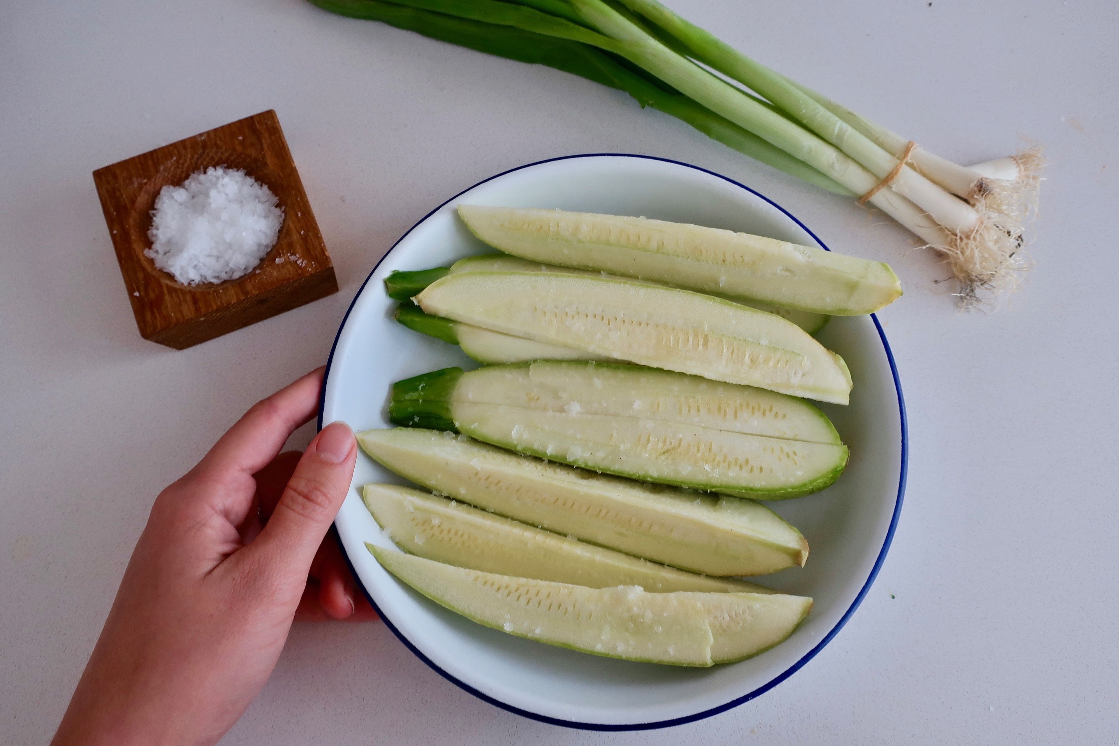 Slice zucchini lengthways. Place in a bowl and sprinkle generously with flaky sea salt to draw out water and season the zucchini. Leave for 15 - 30 min. Rinse and pat dry. Trim root end of the scallions. Transfer to a baking sheet along with the scallions, and two cloves of garlic, skin on. Make a glaze by mixing together the maple syrup and olive oil, plus a pinch of flaky sea salt. brush the zucchini and scallions with half the glaze. Grill in an oven on medium-high, turning as needed and brushing on more glaze. Remove the quicker-cooking scallions first when they are soft and browned. The zucchini will take approx 10 min. to cook and brown a little, depending on the strength of your grill.