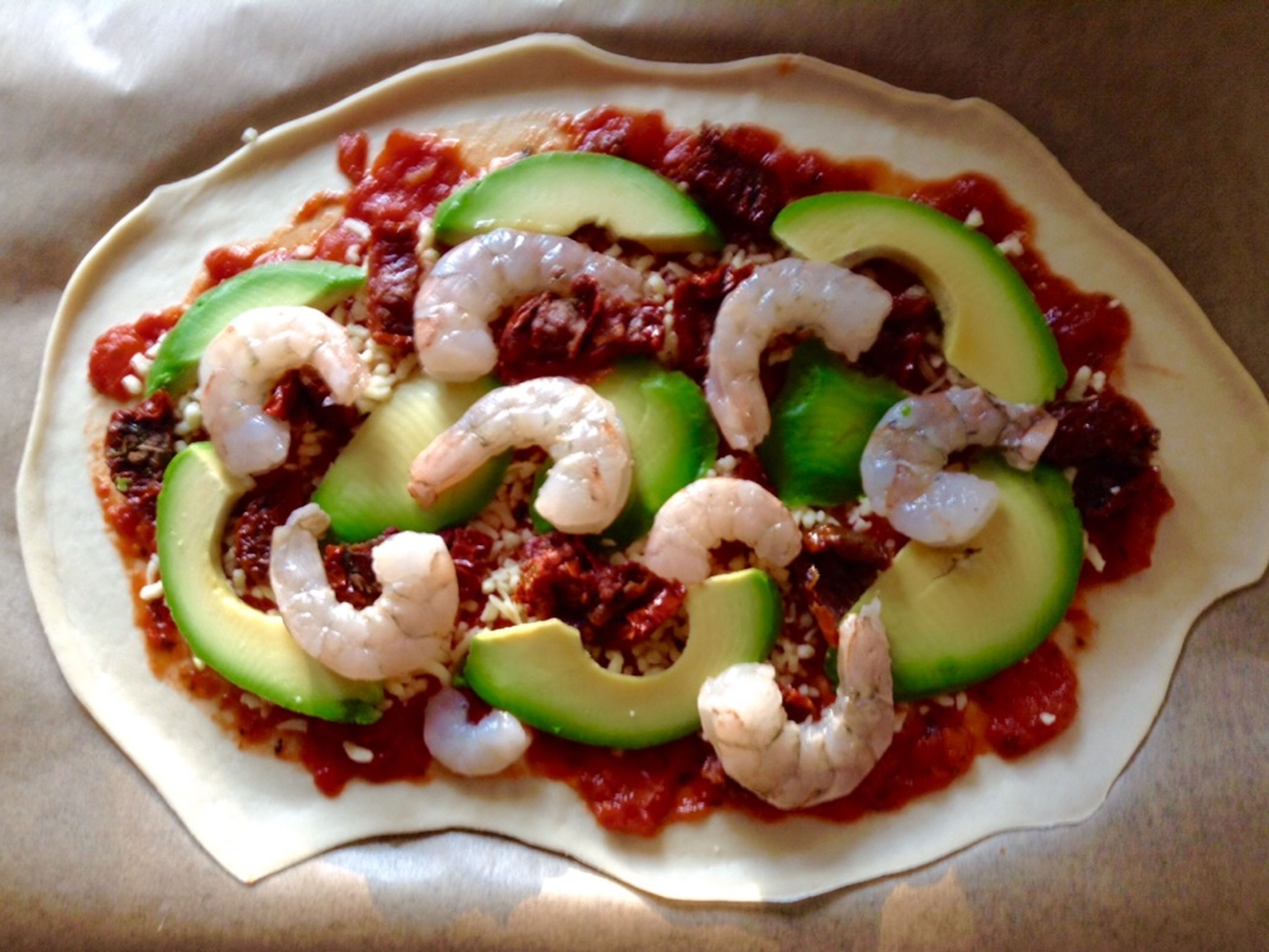 Next, add the toppings. Either put everything on top randomly, or decorate your pizza creatively, as you know—you eat with your eyes first! I started with the avocado (sliced in advance), followed by shrimp (peeled and cleaned beforehand), and finished off with chopped sun-dried tomatoes in the gaps.