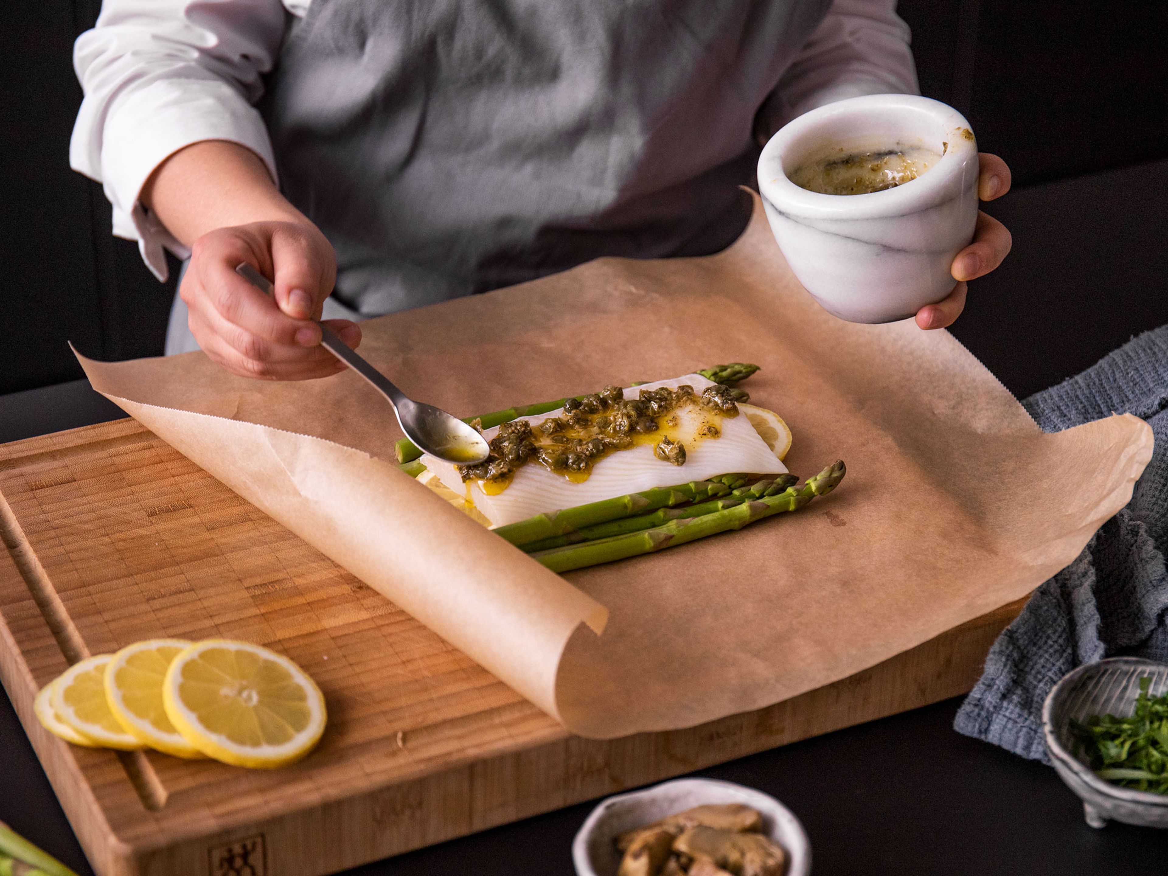 Lay half of the lemon slices on parchment paper with half of the asparagus, halibut fillet, half of the garlic-caper mixture, and half of the artichoke hearts. Fold into a parcel. Repeat with the remaining ingredients on another piece of parchment paper. Carefully transfer parchment parcels to a baking sheet and bake for approx. 15 – 20 min. Delicately open the parchment parcels and top with parsley before serving. Enjoy!