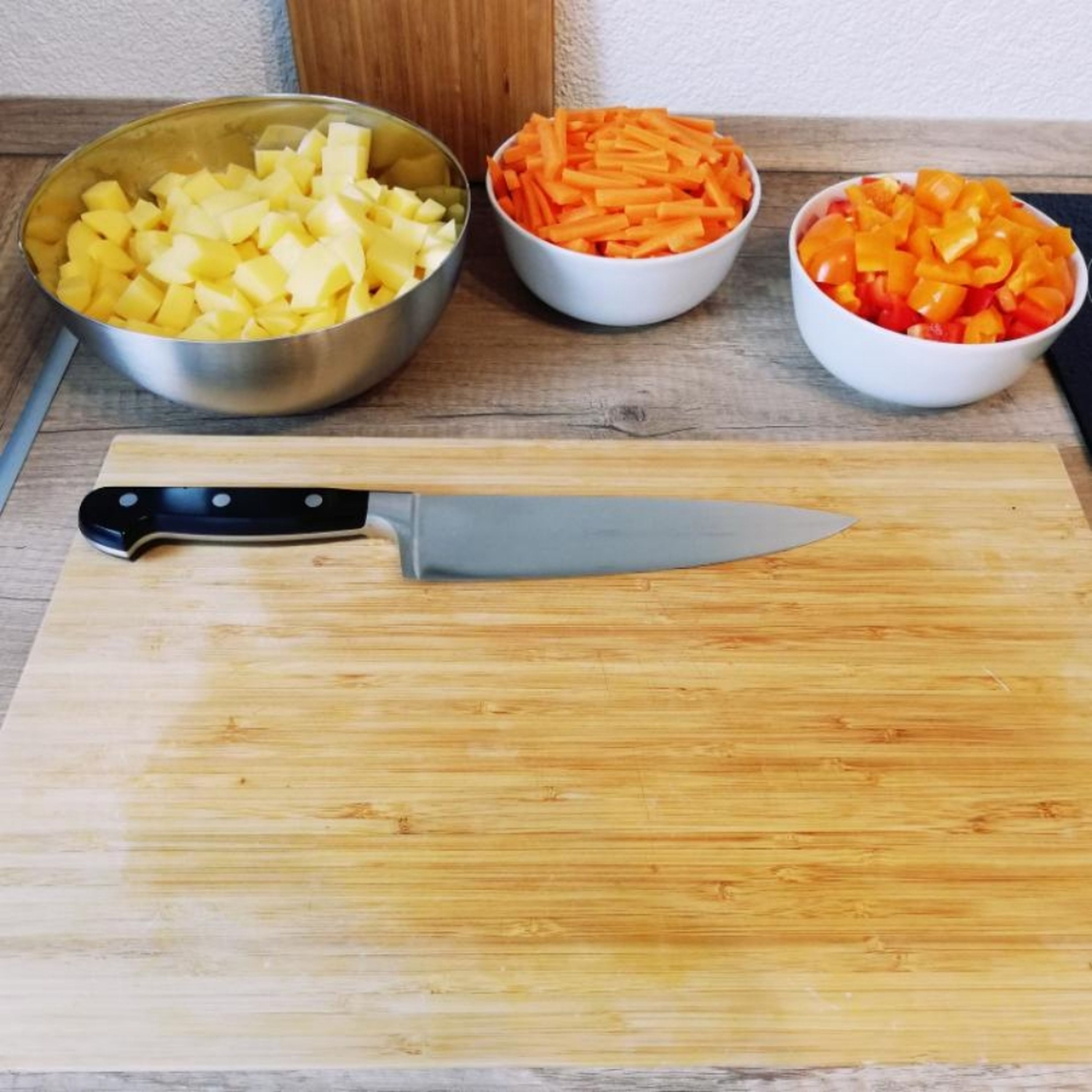 Kartoffeln und Karotten schälen. Kartoffel und Paprika in Würfel und Karotten in Streifen schneiden. Gemüse zum Gulasch geben. Alles für weitere ca. 20 – 30 Min. köcheln lassen.