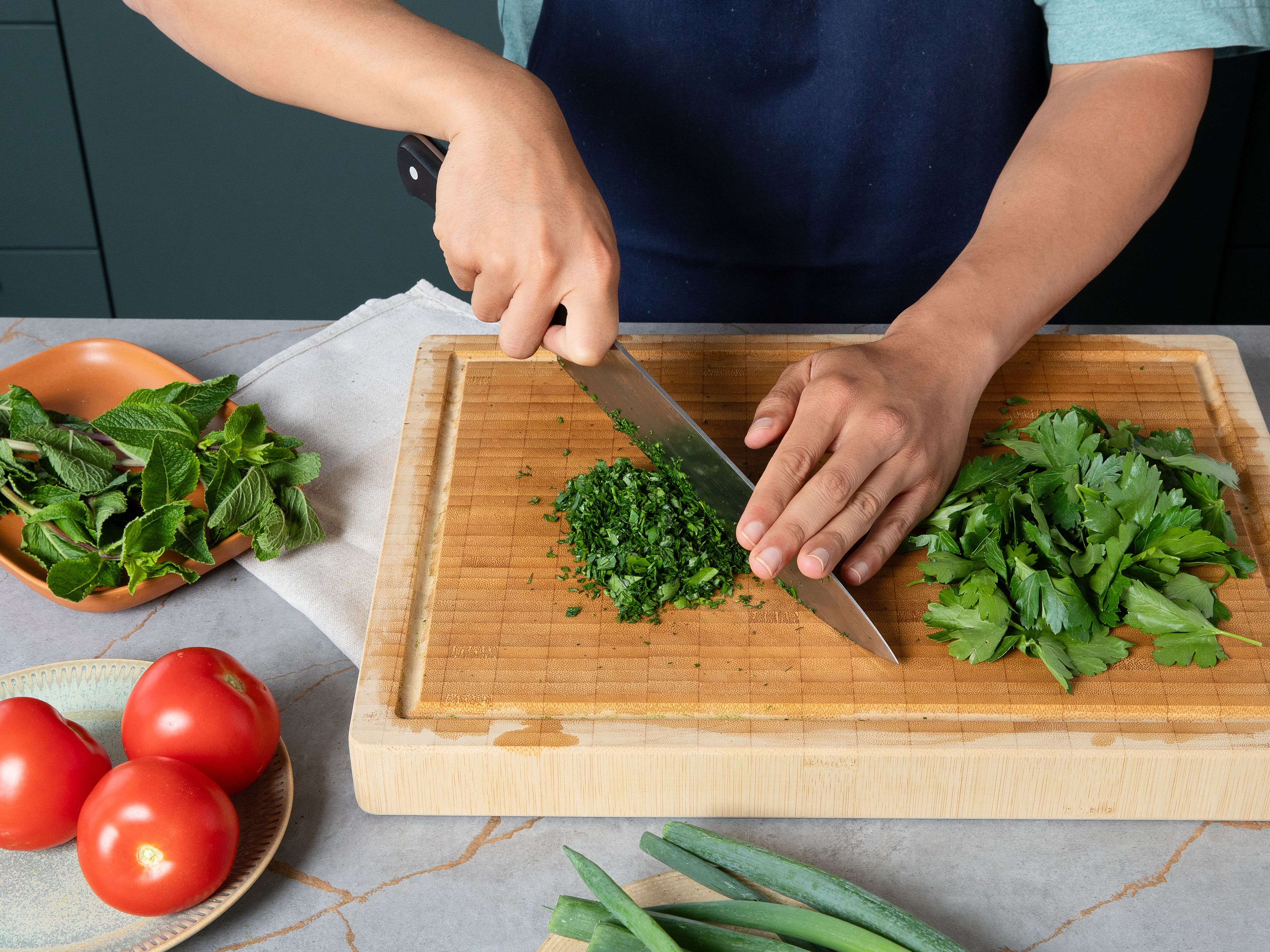 Die Stiele von Petersilie und Minze entfernen, dann die Blätter fein hacken oder mit einer Küchenmaschine zerkleinern. Die Frühlingszwiebeln in feine Ringe schneiden. Die Tomaten vierteln, entkernen und das wässrige Innere entfernen und dann würfeln. Alle Zutaten in eine große Schüssel geben, vermengen und mit Salz und Pfeffer würzen.