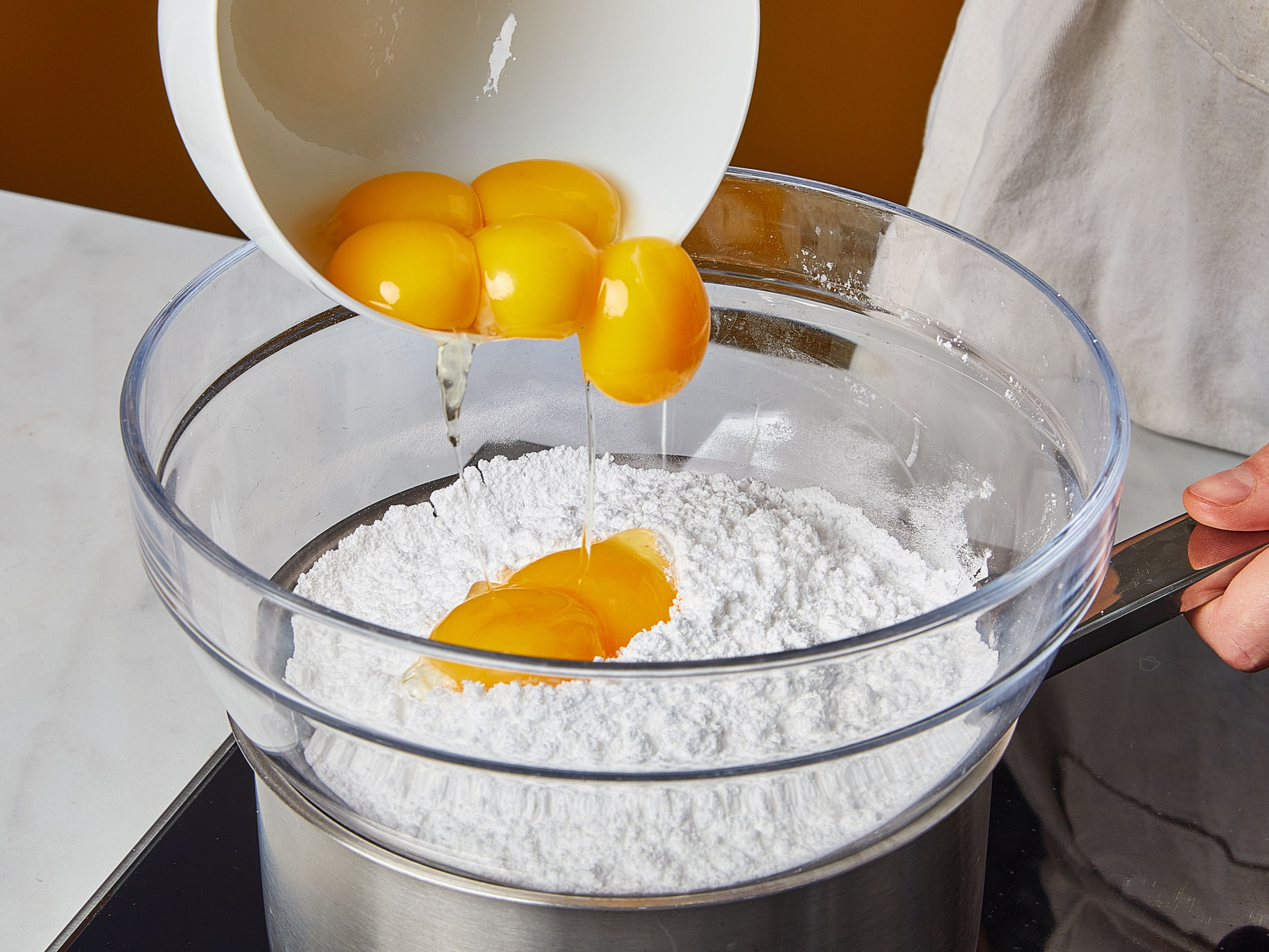 For the water bath (bain-marie), fill a pot with a few inches of water and set on medium to low heat, so it barely boils. Sift confectioner's sugar into a heatproof round-bottomed bowl. Place the bowl over the pot so that the bowl sits well on the rim but does not touch the water. Add egg yolks to the bowl and whisk immediately in the bain-marie (approx. 60°C/140°F) using a whisk or hand mixer until everything is thick and smooth. Make sure that the yolks do not curdle by stirring constantly and not letting the mixture get too hot.