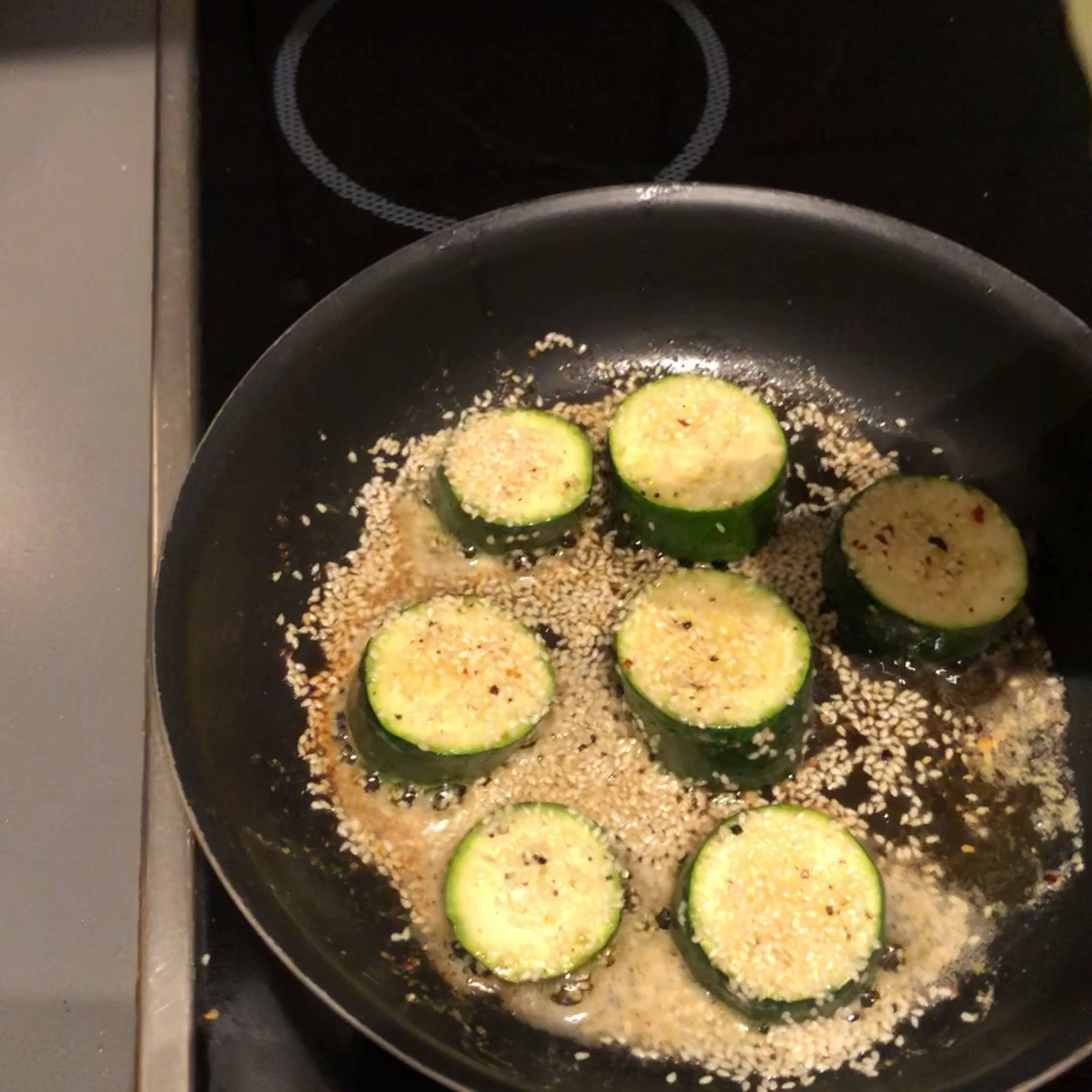 Ein Stück Butter in einer Pfanne zum schmelzen bringen. Danach die Zucchini Taler hinzugeben und unter gelegentlichen Wenden auf leichter Stufe anbraten (ca 10-15 Minuten). Während des Bratens, mit Salz und Pfeffer würzen und mit Sesam versehen.