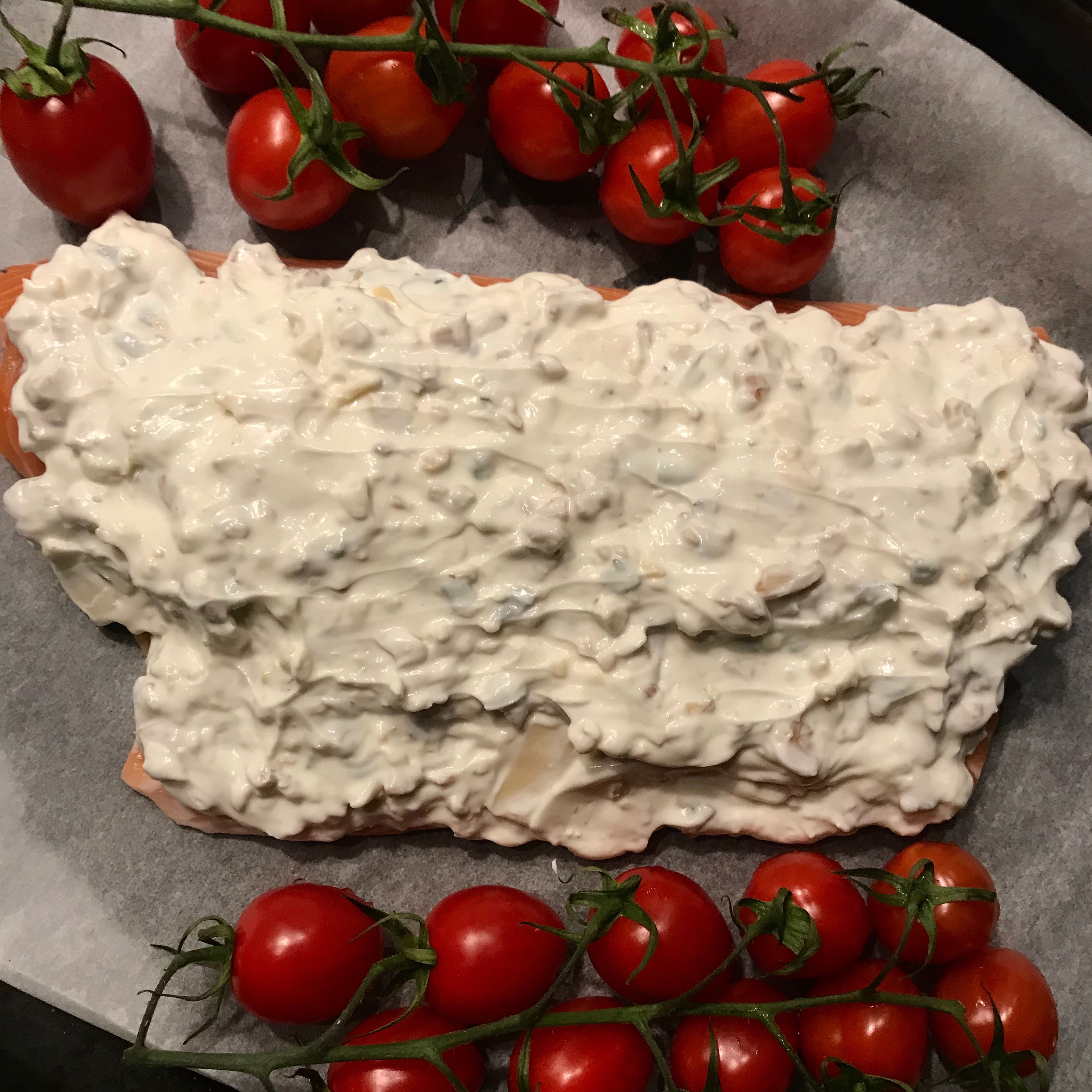Place the salmon fillet on a baking paper sheet on an oven tray. Spread the yoghurt mix over the fillet. Place the tomatoes to the sides of the fillet.